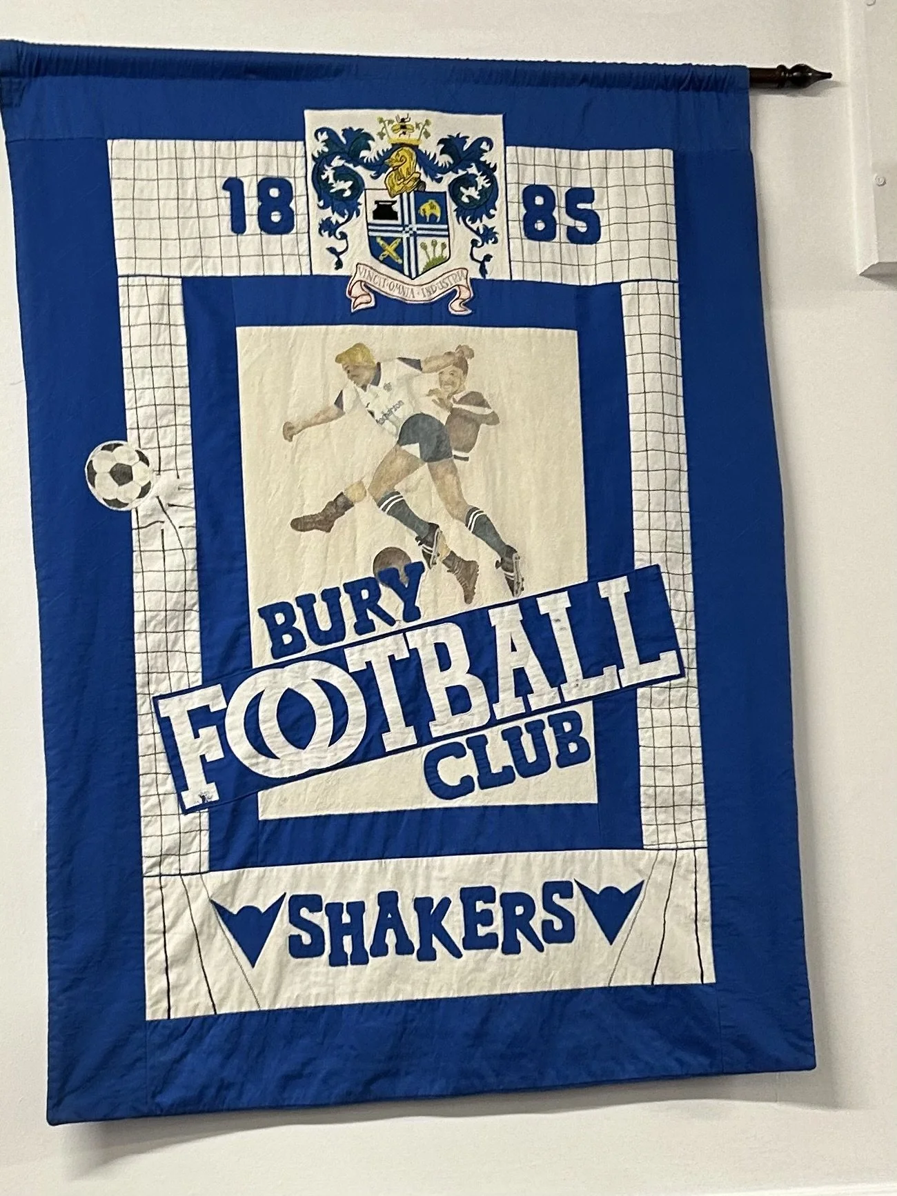 Bury Football Club banner with images of two football players and the words 'Bury Football Club Shakers', featuring a crest with the year 1885 and a soccer ball.