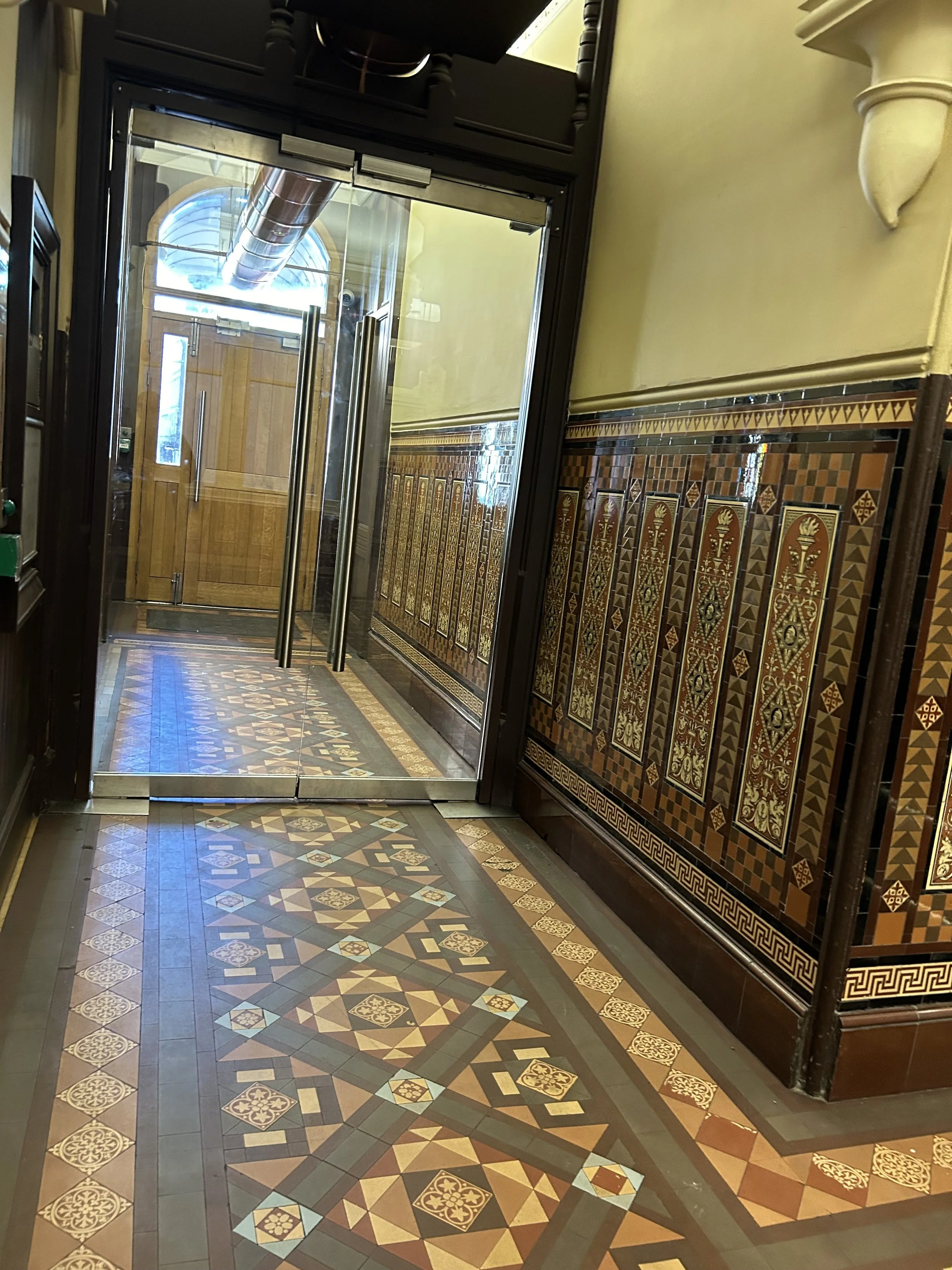 Decorative tiled floor and ornate wall paneling near a glass door with metal handles in an interior space.