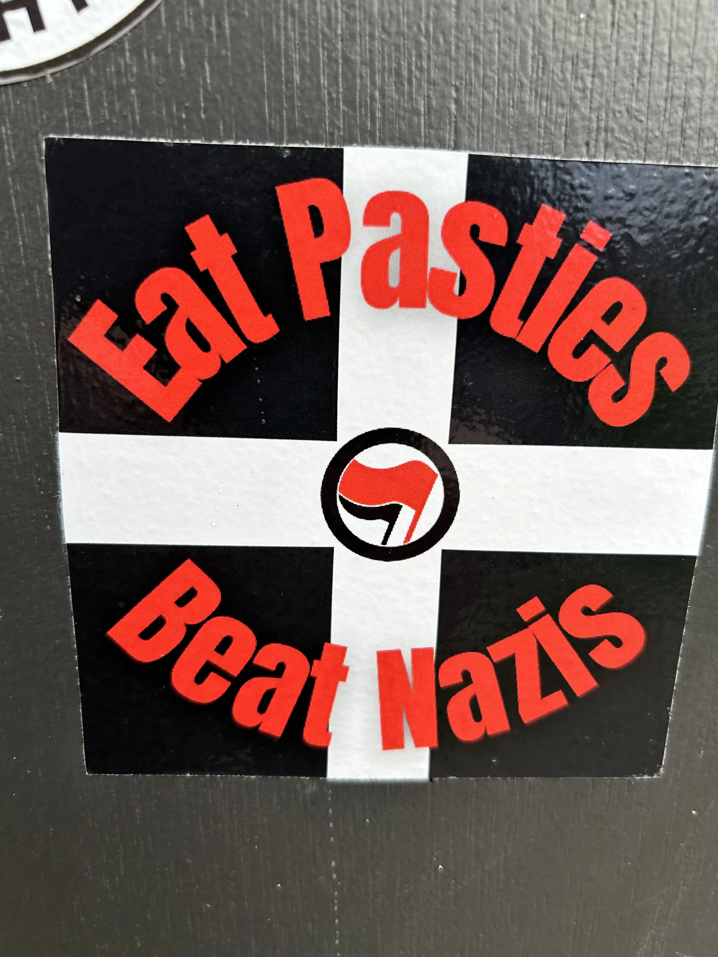 Sticker with black and white cross background, red text saying 'Eat Pasties' and 'Eat Nais' around a logo in the center.