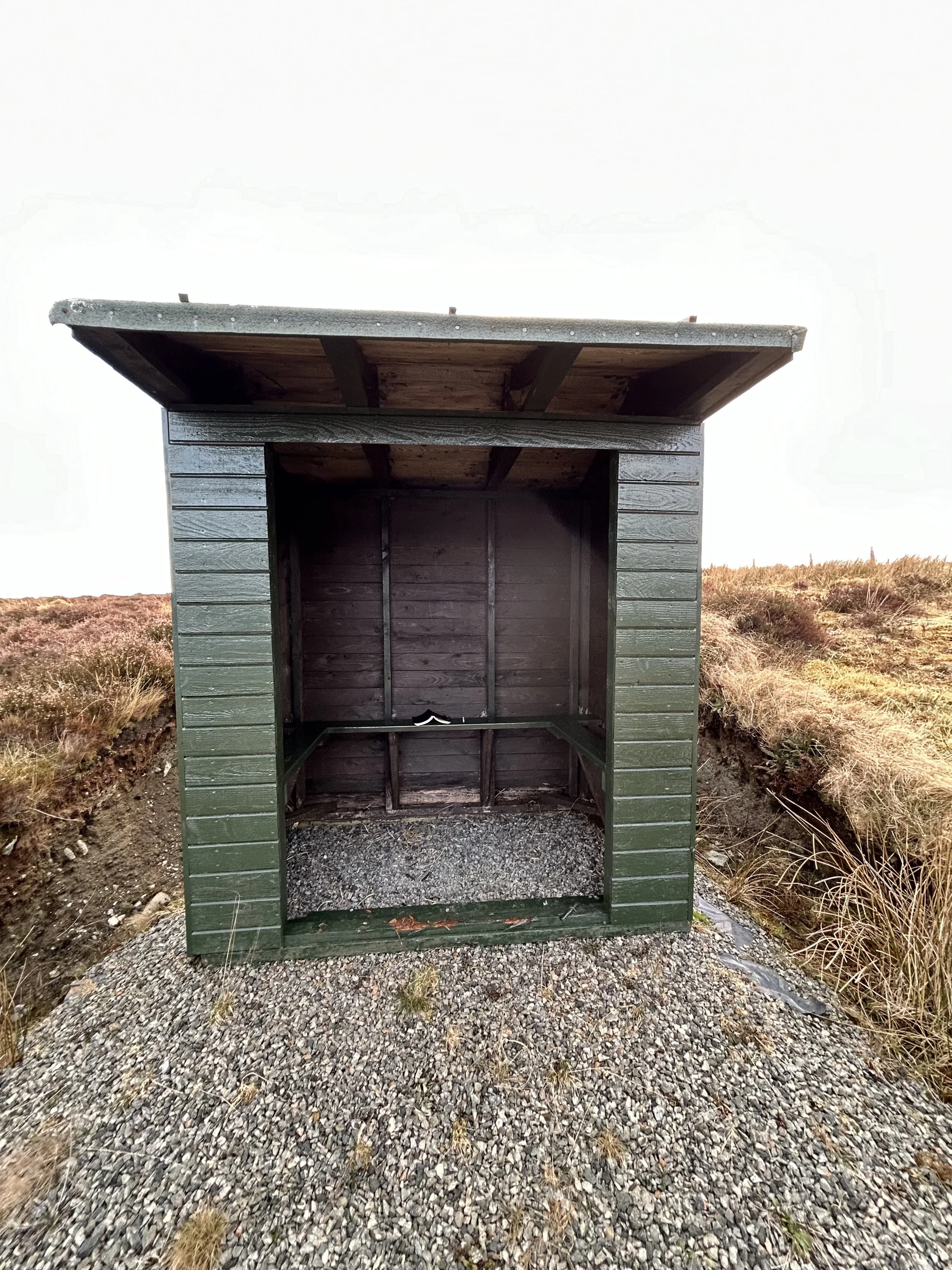Empty green wooden shelter on gravel path in open grassy field