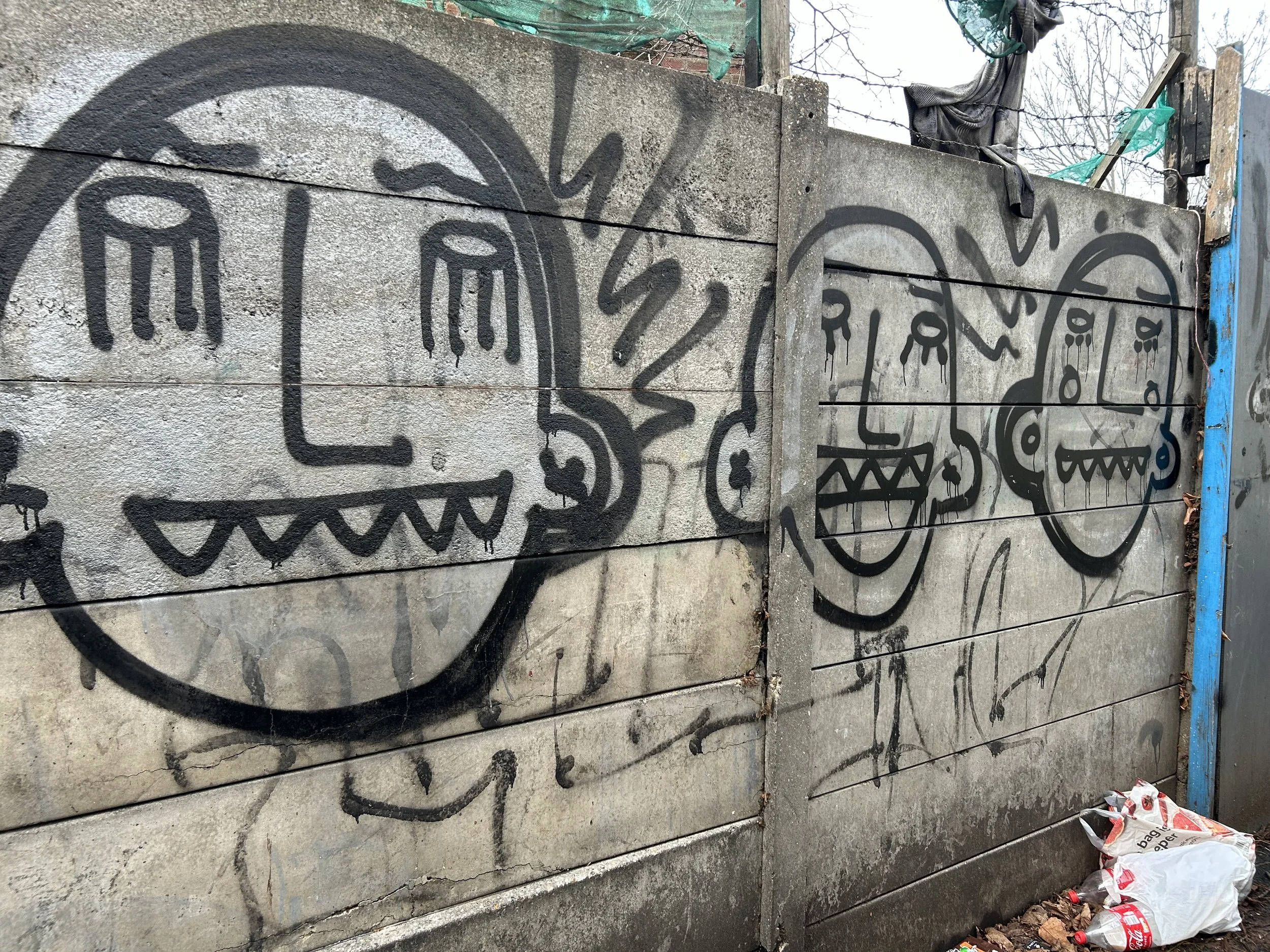 Graffiti art on a concrete wall depicting three cartoonish monsters with sharp teeth and wide mouths. The first monster is drawn with a big head and has two antennae, the second has a round head with bells hanging on its face, and the third has a lar