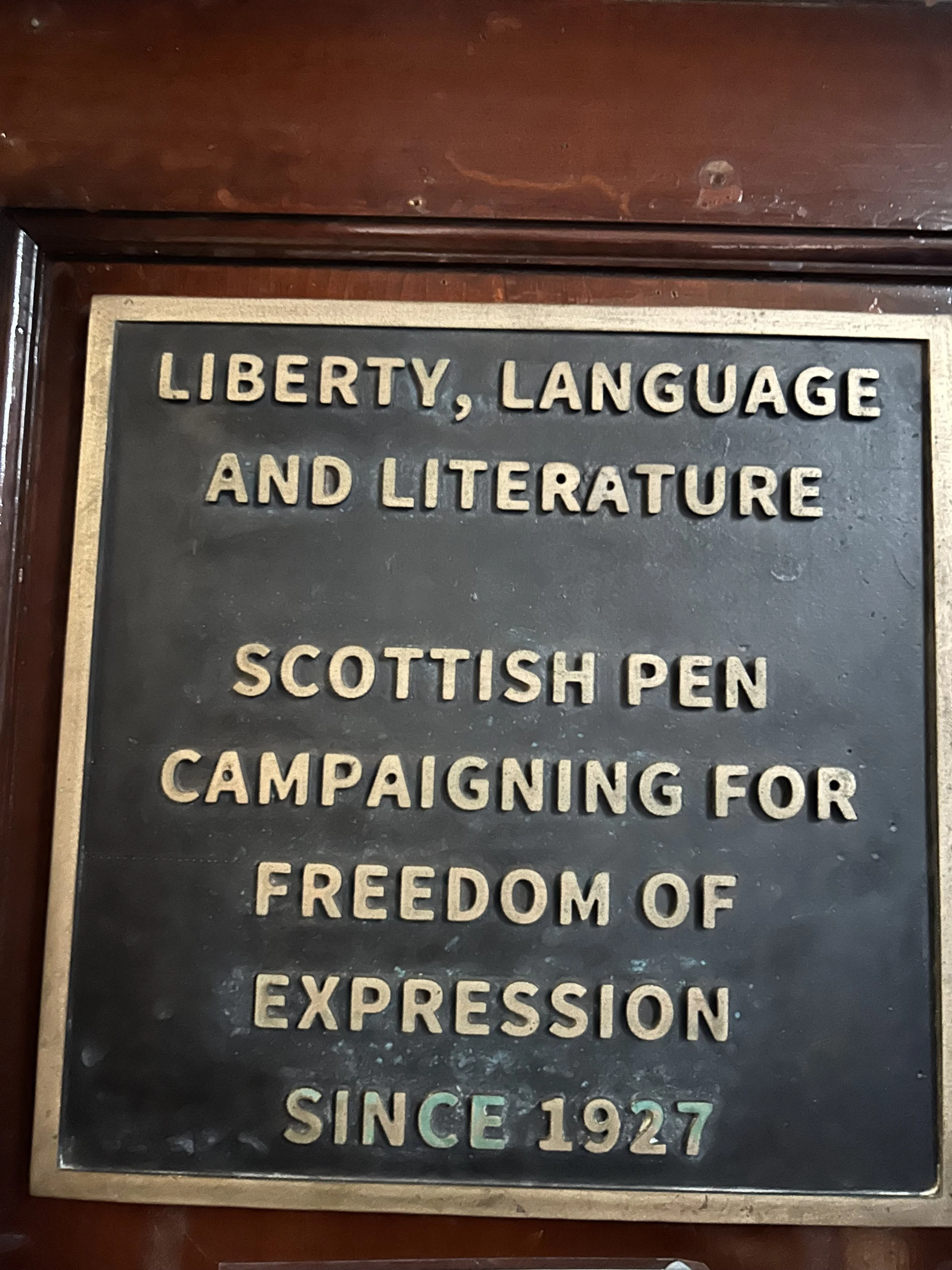 A black and gold plaque with raised lettering that reads, "Liberty, Language and Literature. Scottish Pen Campaigning for Freedom of Expression Since 1927."