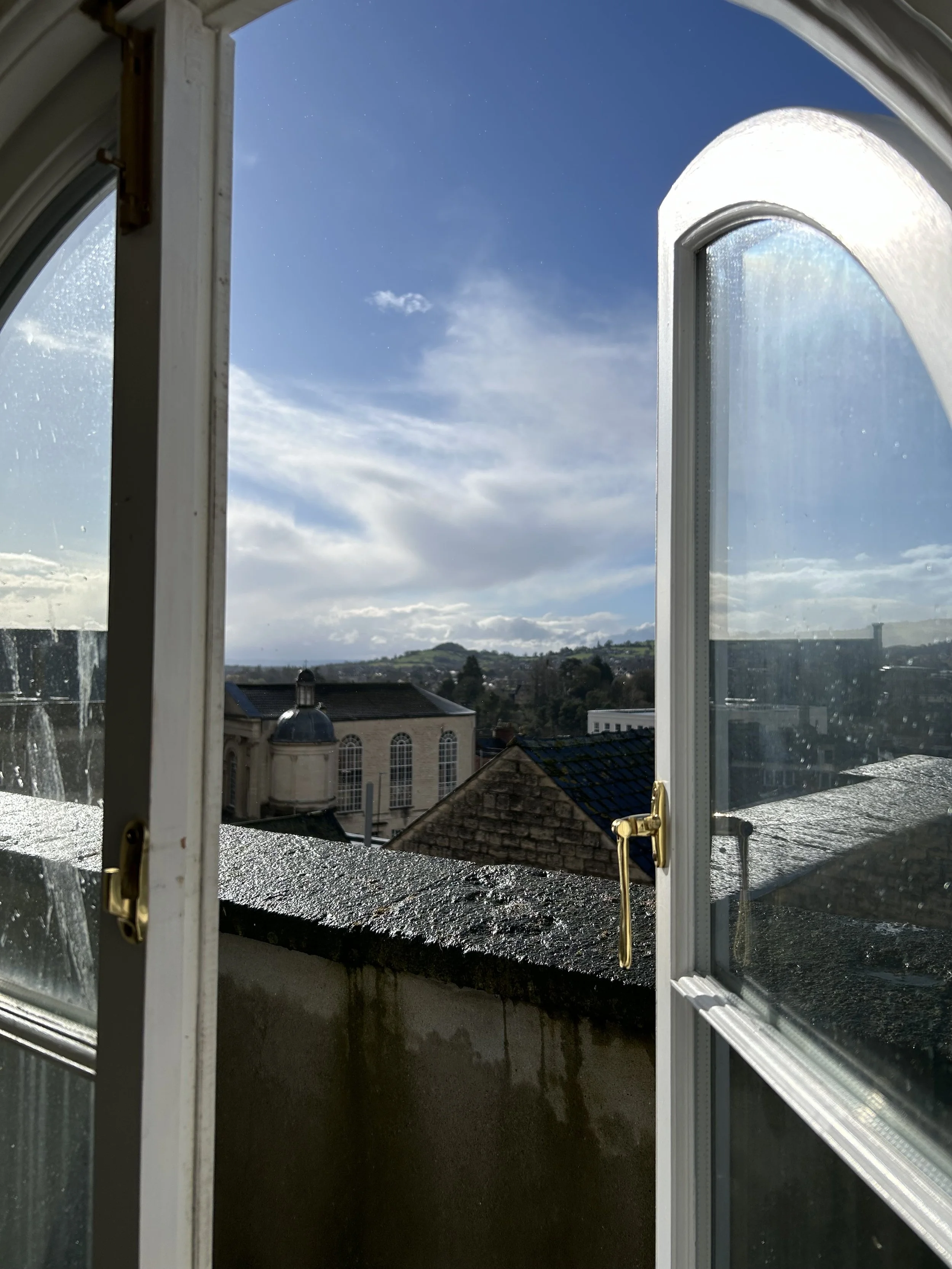 Open window overlooking rooftops and a cloudy sky.