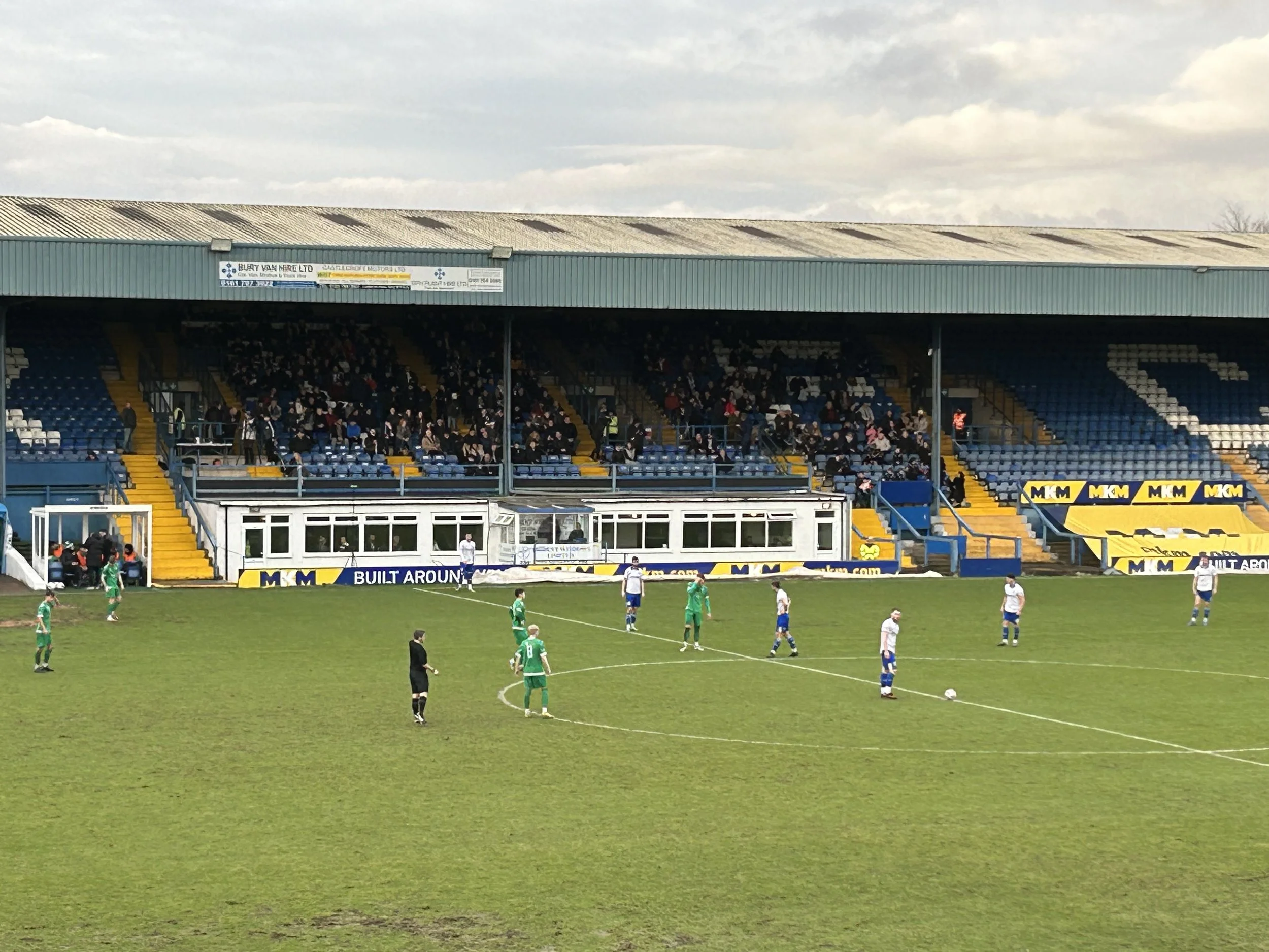 A soccer match in progress with players on the field and spectators in the stands of a stadium.