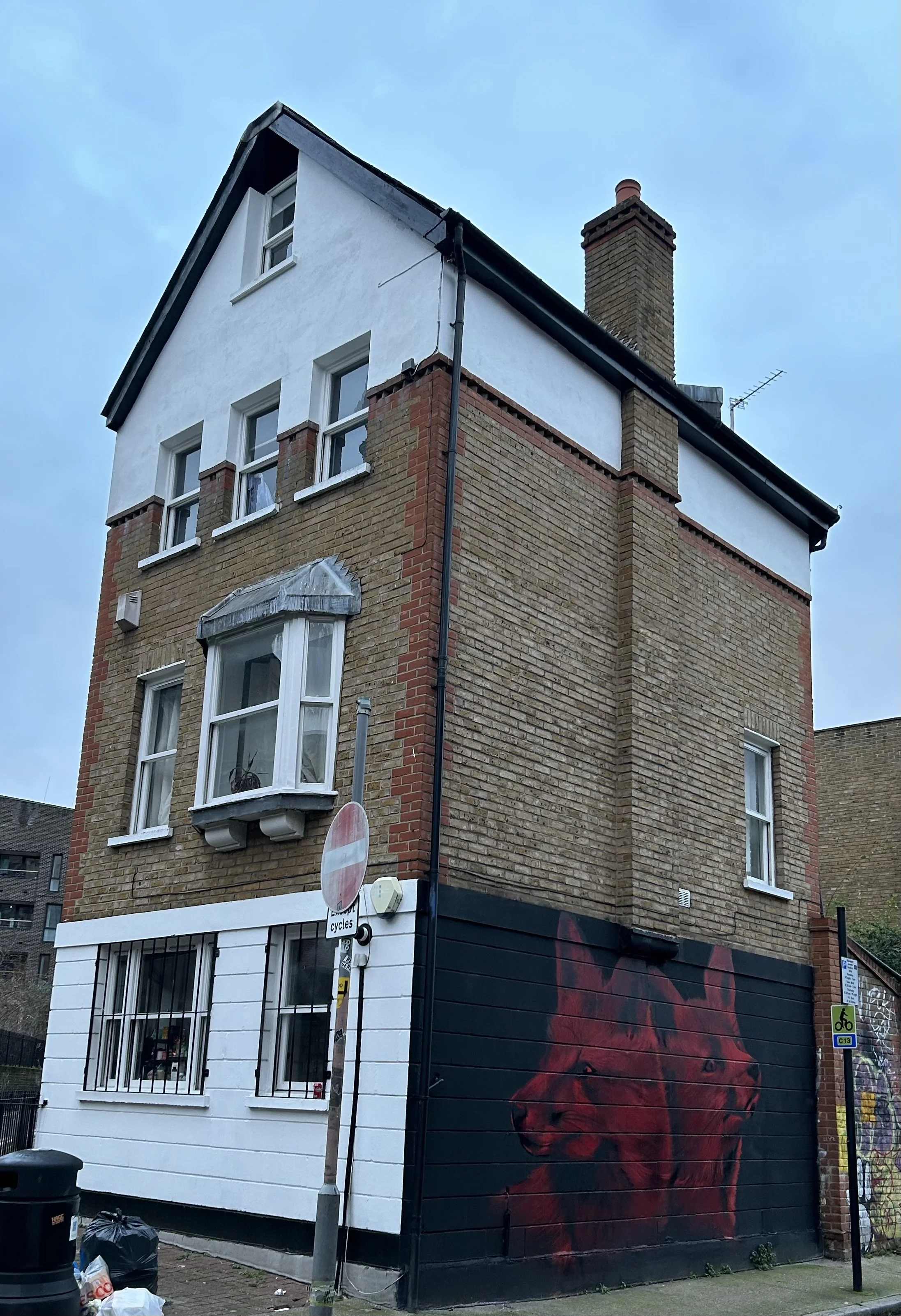 Multi-story brick building with a mural of a red lion on the lower section of the wall, street signs, and graffiti.
