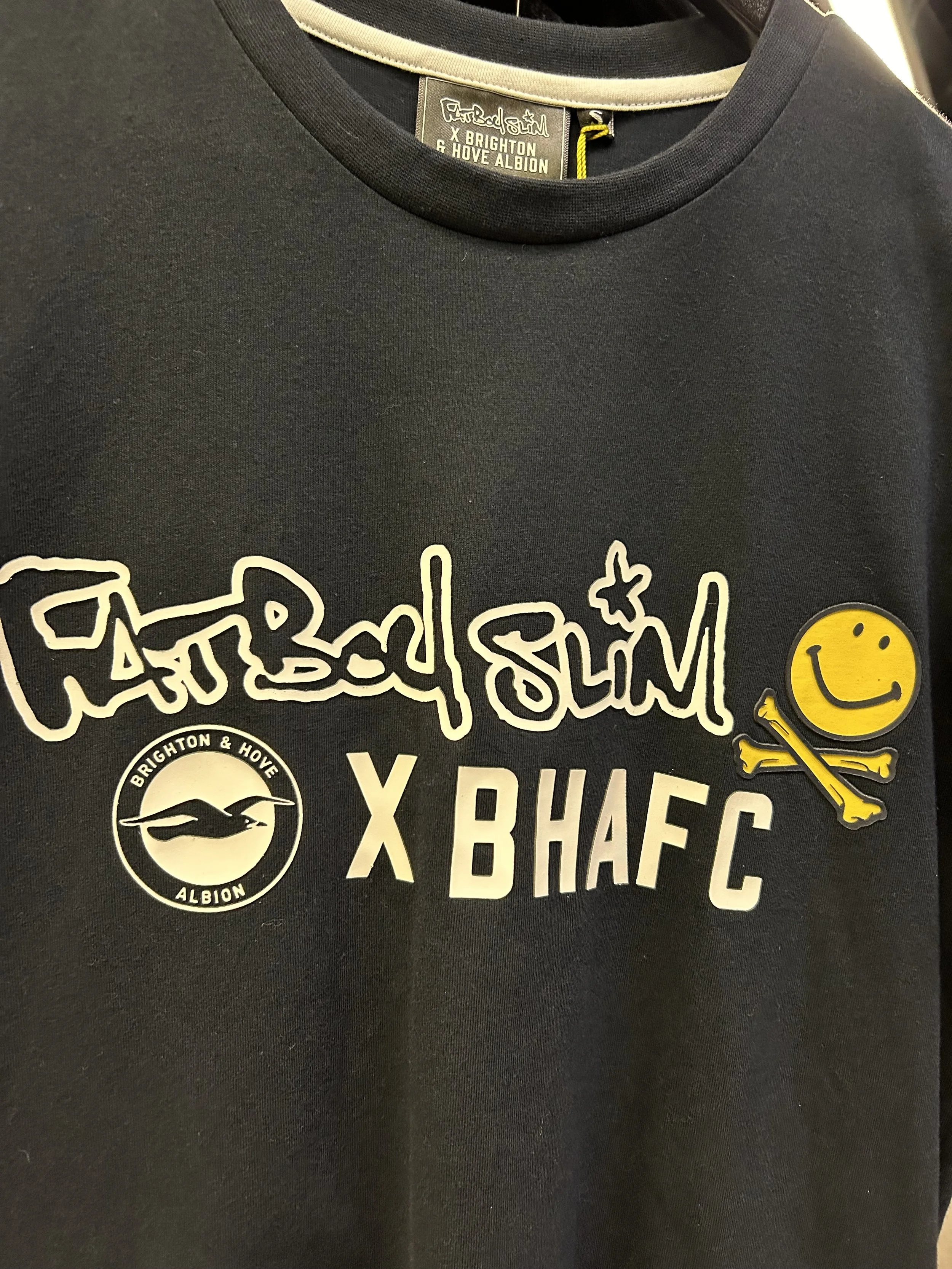 Black Durham City T-shirt with Chelsea Football Club and Brighton & Hove Albion Football Club logos, and a yellow smiley face with a crossbones design.