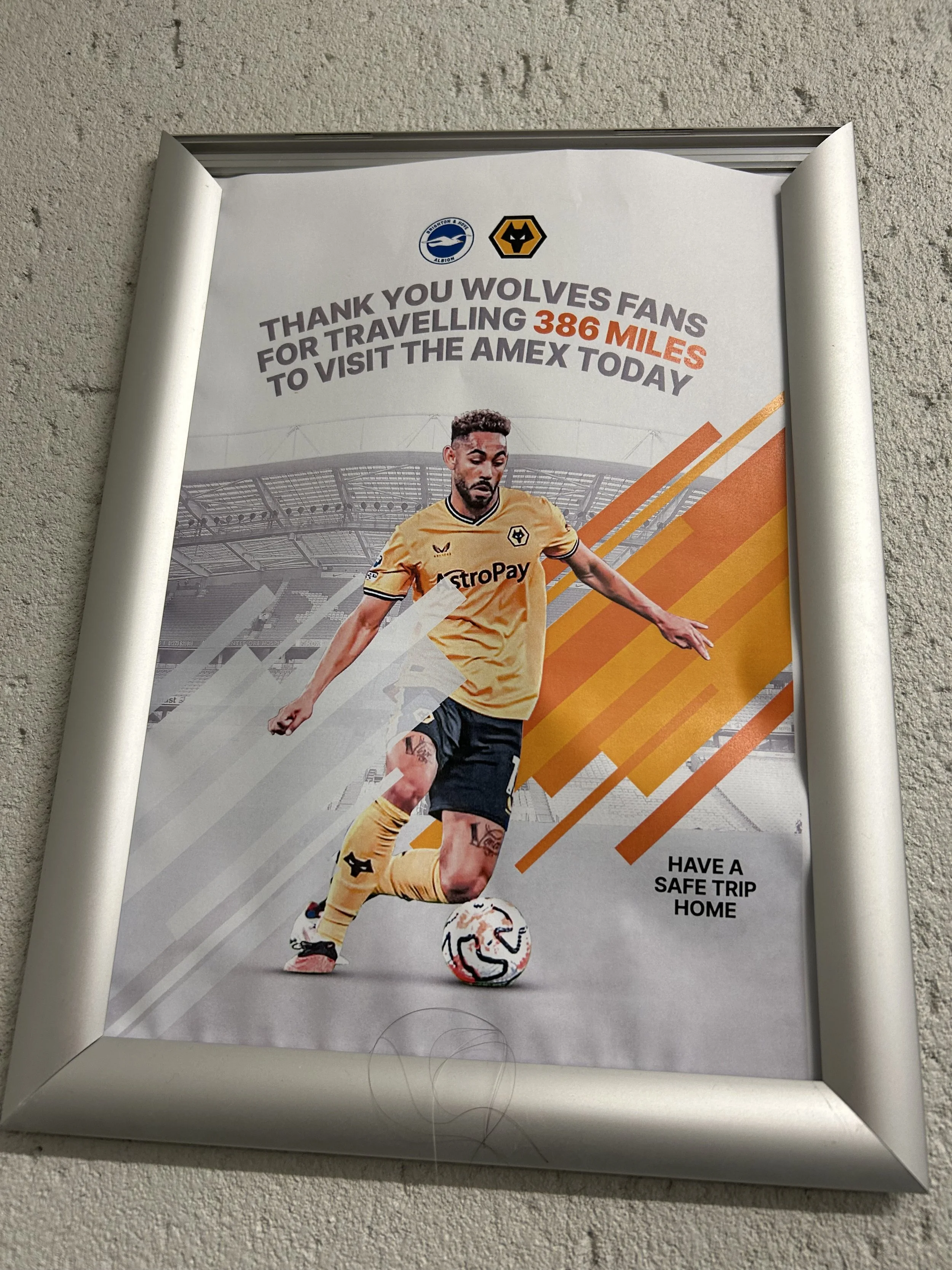 Framed poster thanking Wolves fans for traveling 386 miles to visit the AMEX stadium, featuring a soccer player in a yellow jersey, with a soccer ball at his feet, and the text 'Thank you Wolves fans for travelling 386 miles to visit the AMEX today' 