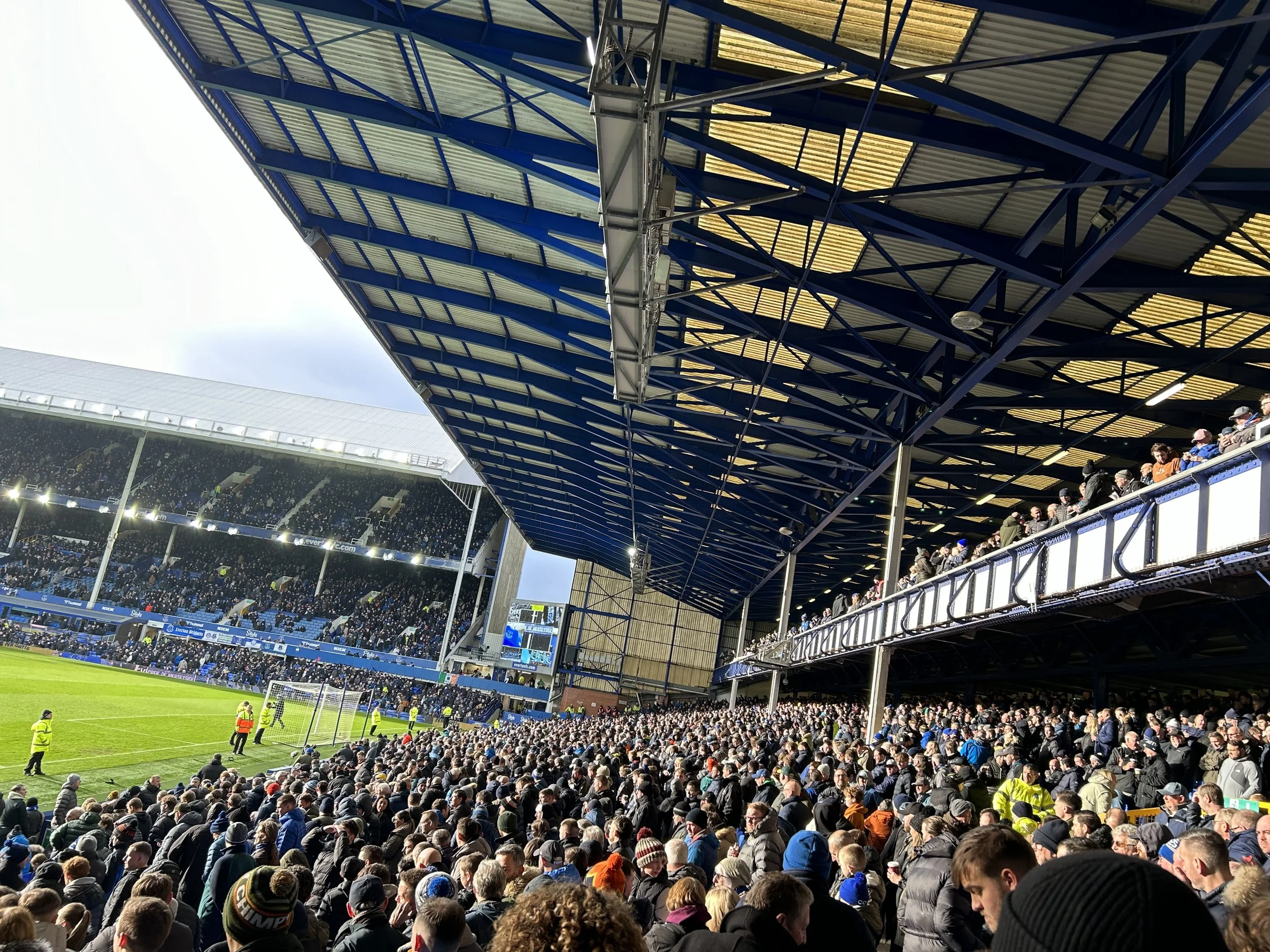 Crowd attending a soccer game at a stadium with a large covered seating area and a lush green field.