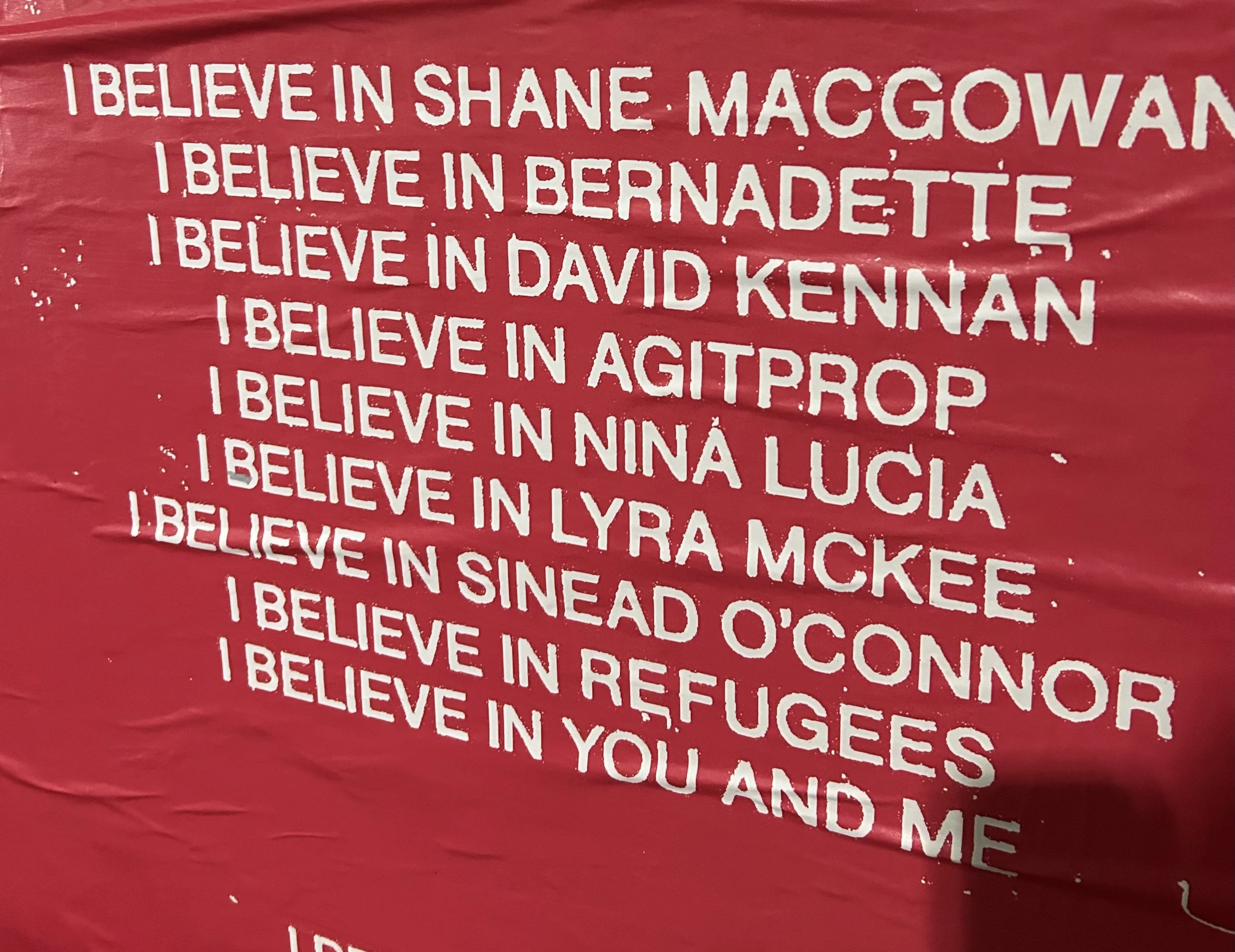 Red background with white painted text listing names of individuals followed by 'I believe in' and their names.