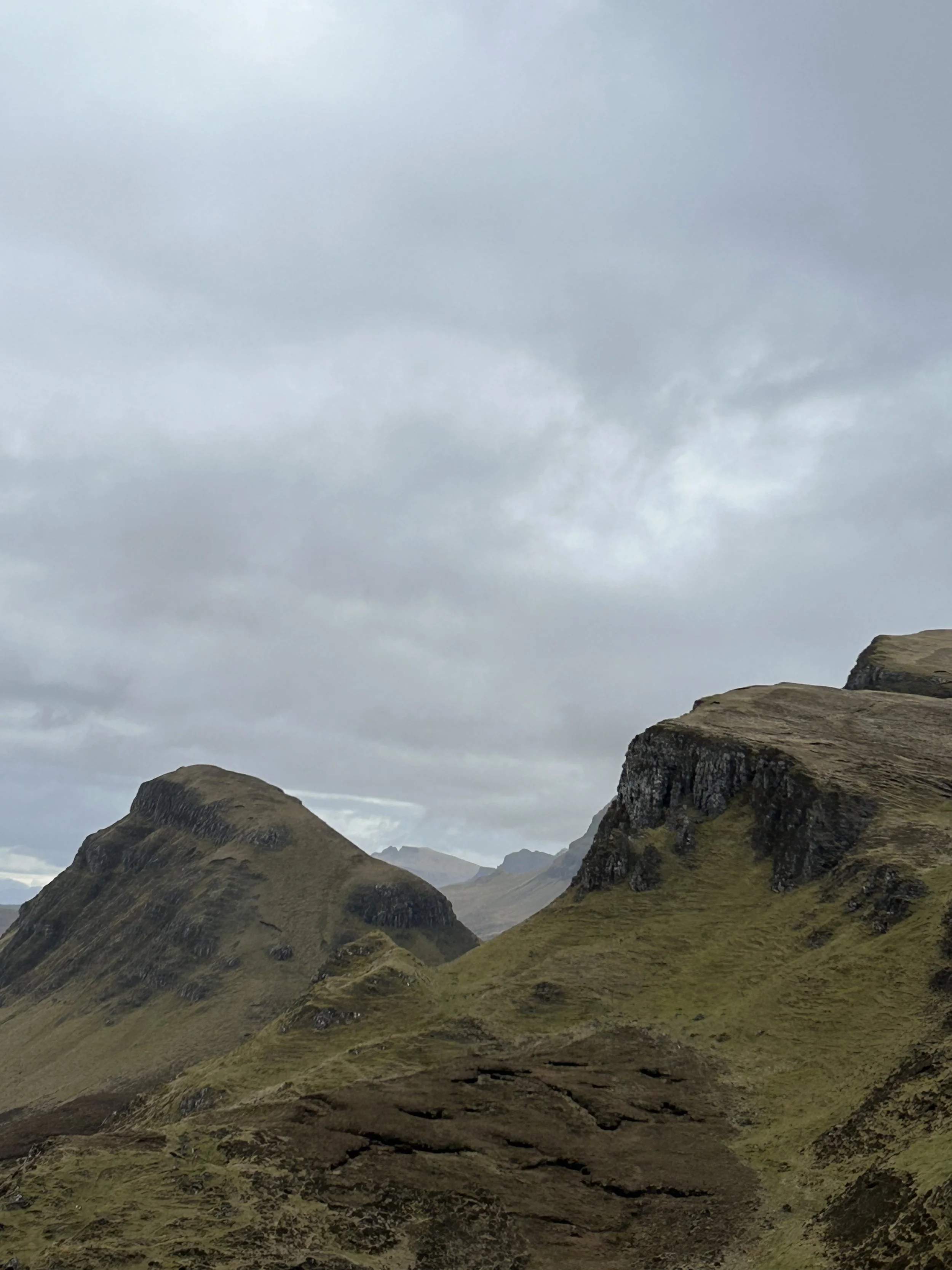 A landscape of rolling green hills with rocky formations under a cloudy sky.