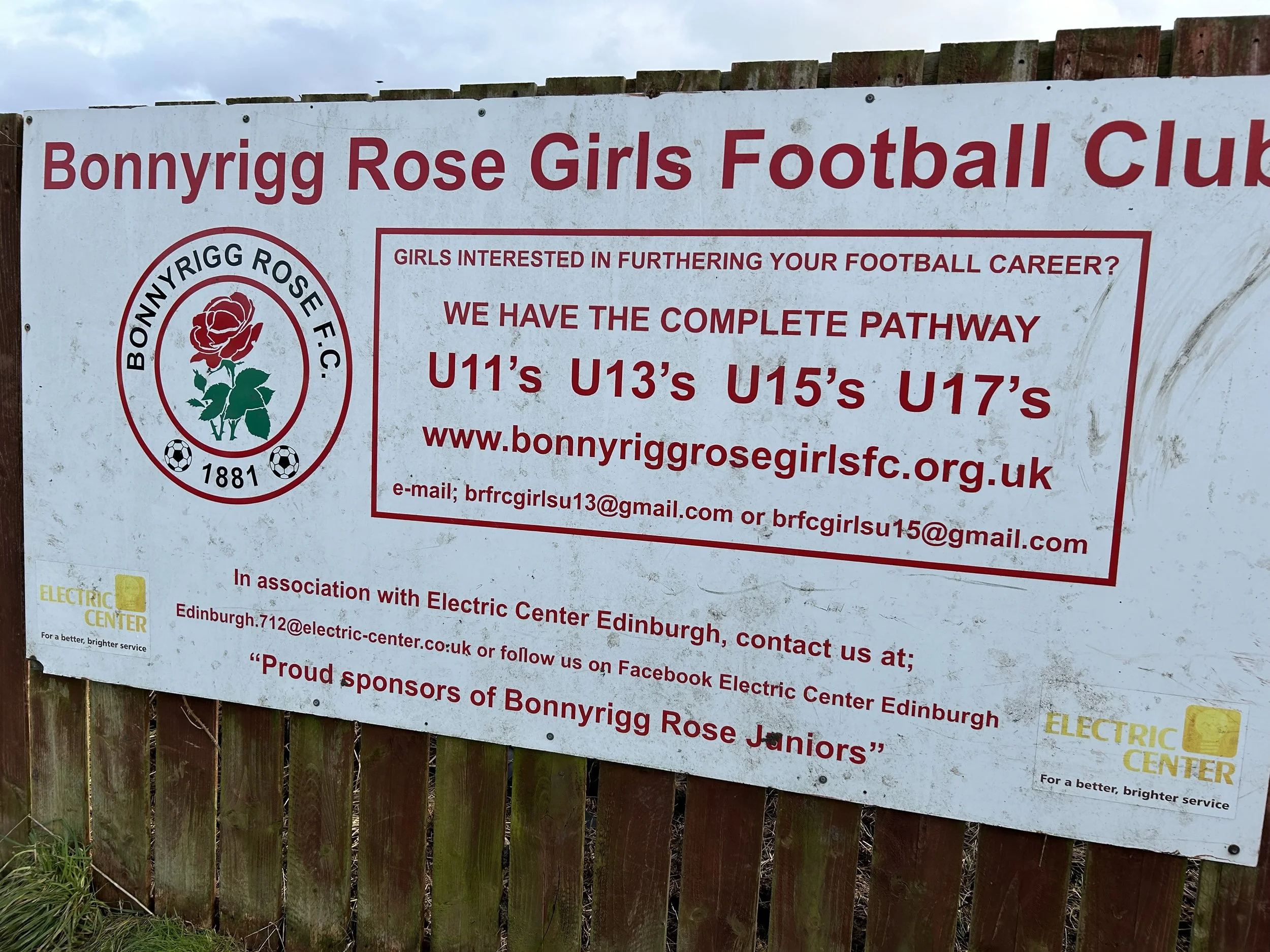 Signboard for Bonnyrigg Rose Girls Football Club with club logo, contact information, and sponsorship details.