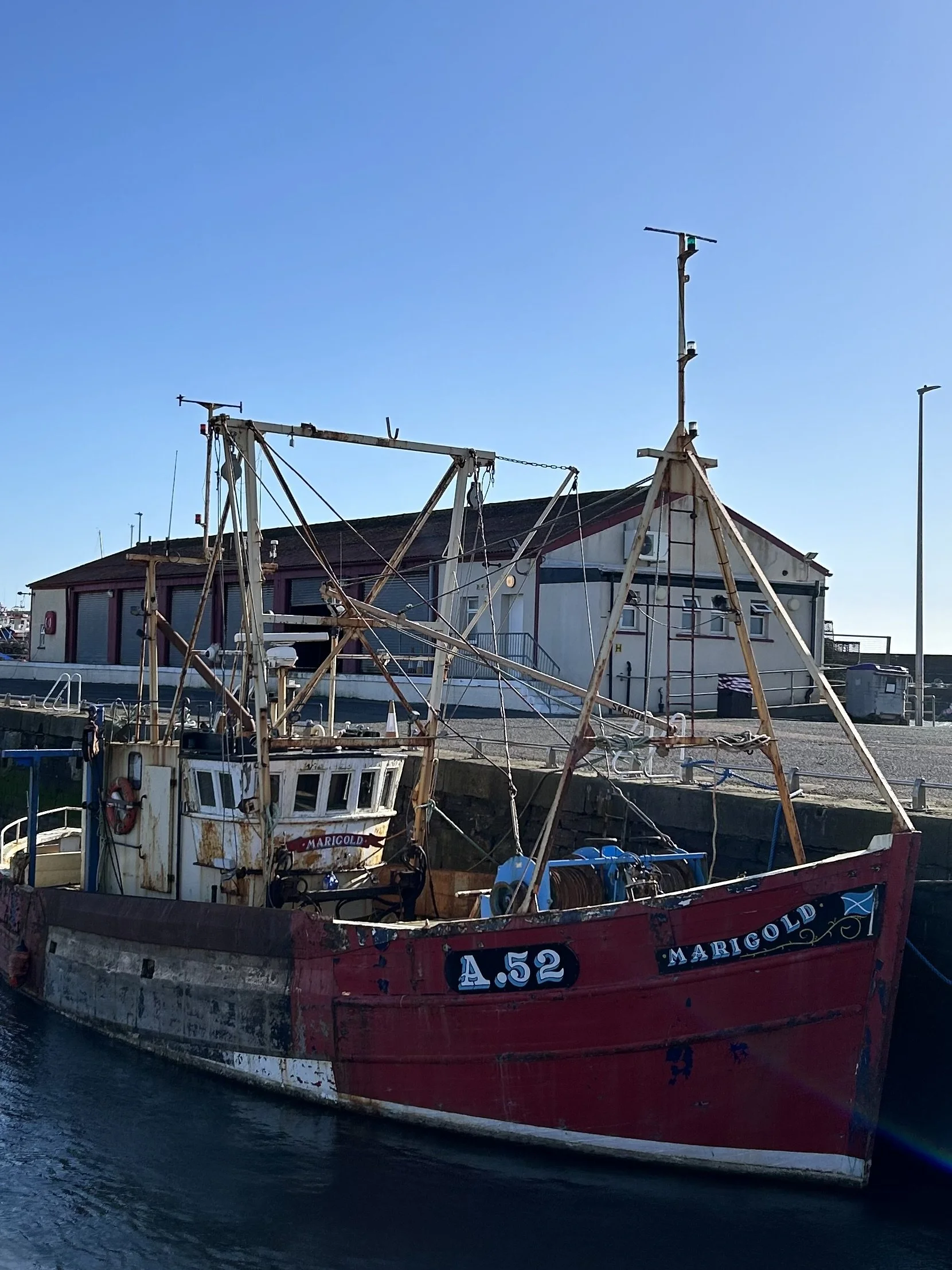 An old fishing boat named 'Marigold' docked at a harbor with a building and clear blue sky in the background.