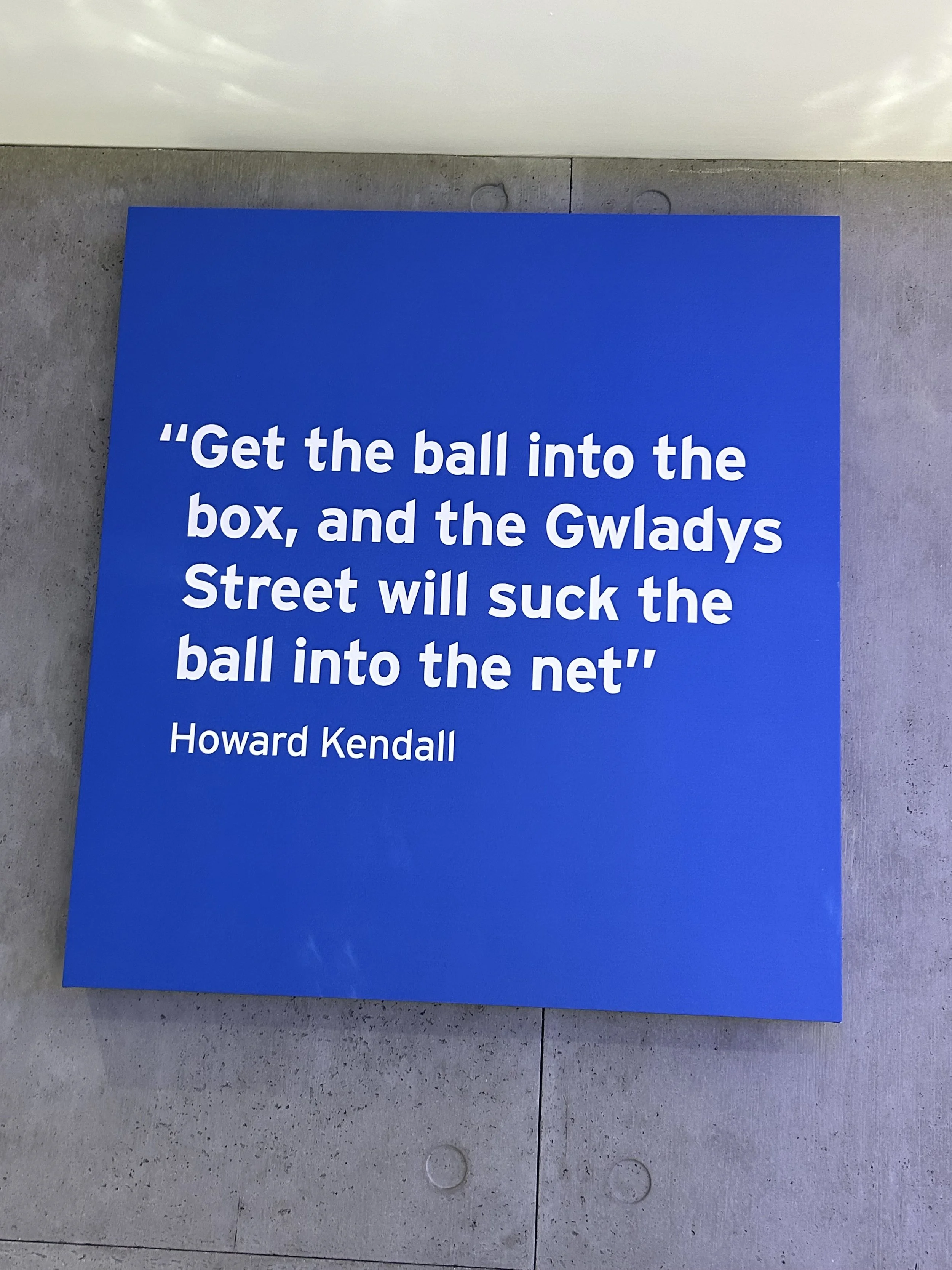 Blue sign with a quote by Howard Kendall that says, 'Get the ball into the box, and the Gwlady's Street will suck the ball into the net.'