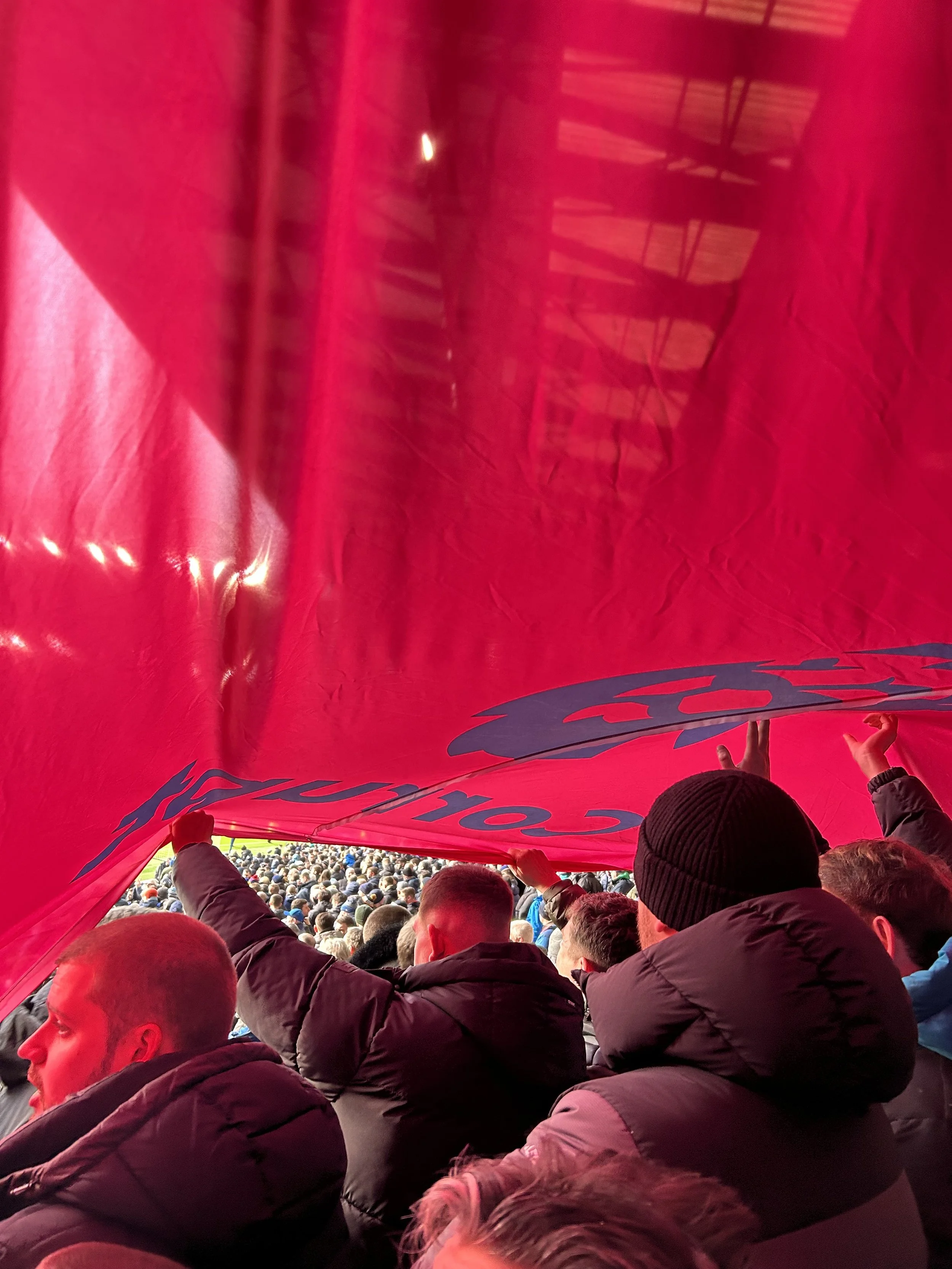 Crowd of spectators at a sporting event, some holding a large red banner overhead.