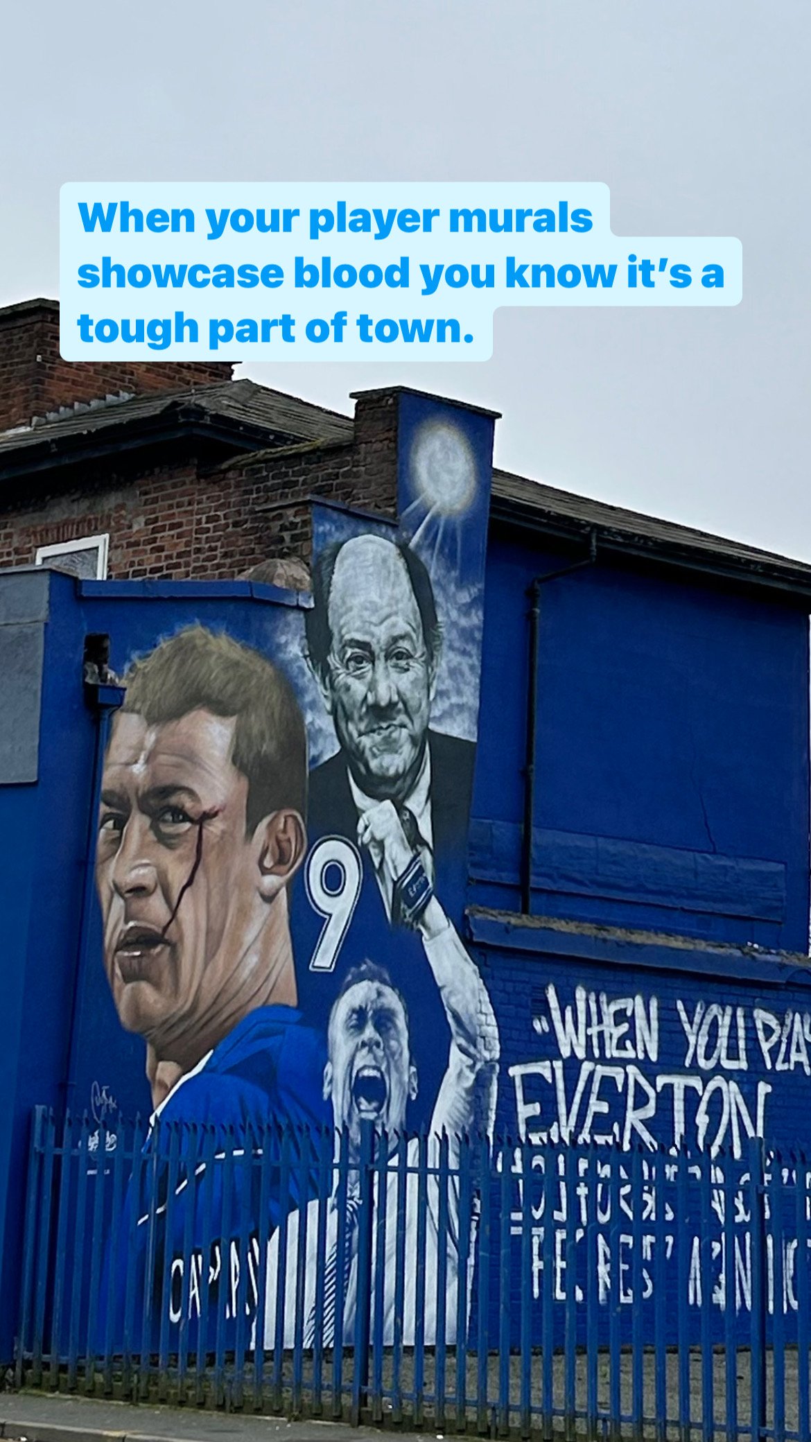 A vibrant blue mural on a wall showcasing portraits of soccer players, including one with a bloodied face and an aggressive expression, and another smiling. The mural features the quote, 'When your player murals showcase blood you know it’s a tough p