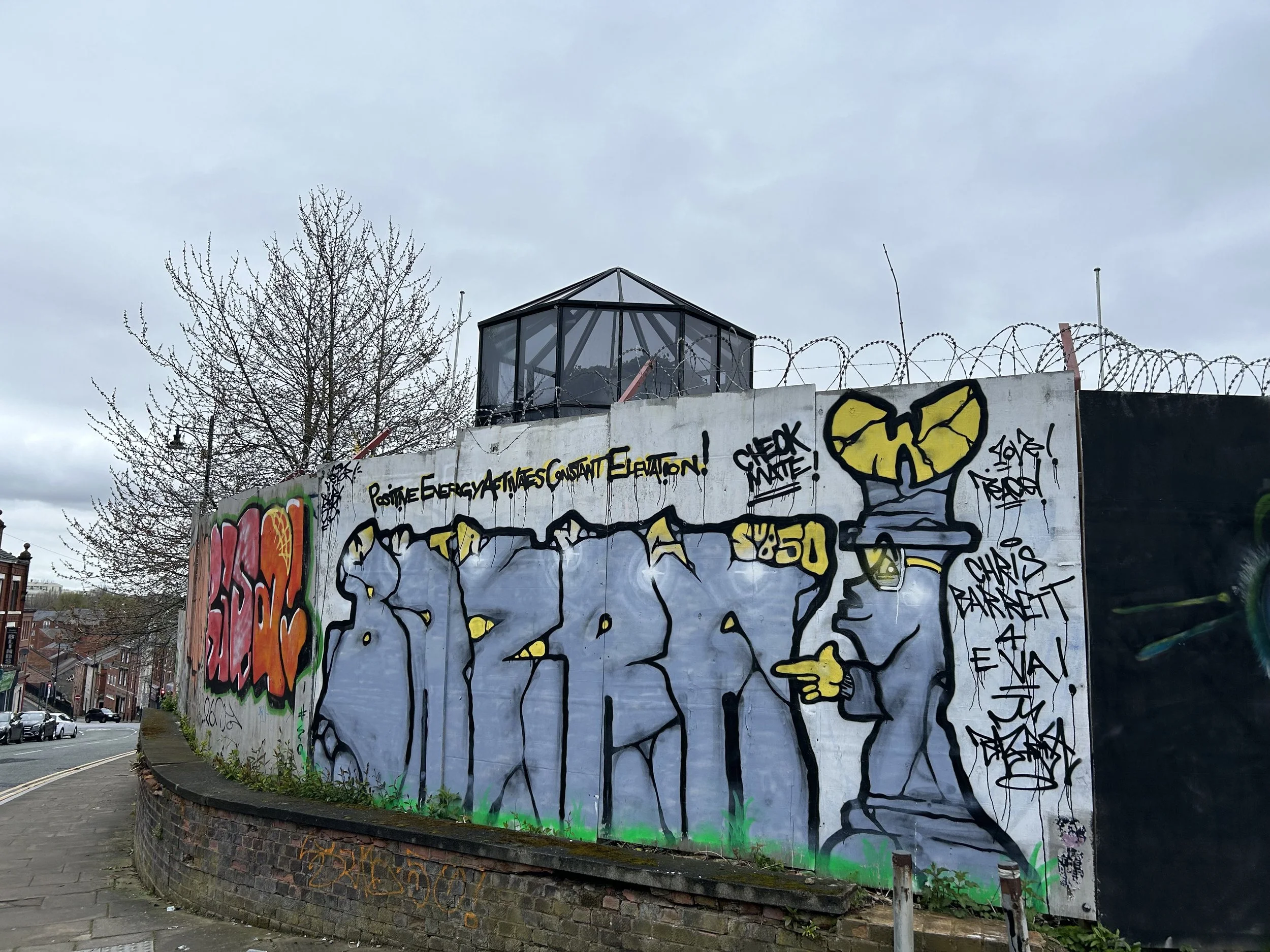 Street art graffiti on a concrete wall featuring colorful lettering, a character with a heart-shaped head pointing, and tags with words like 'CHECK WAVE!' and 'SK8 50'.