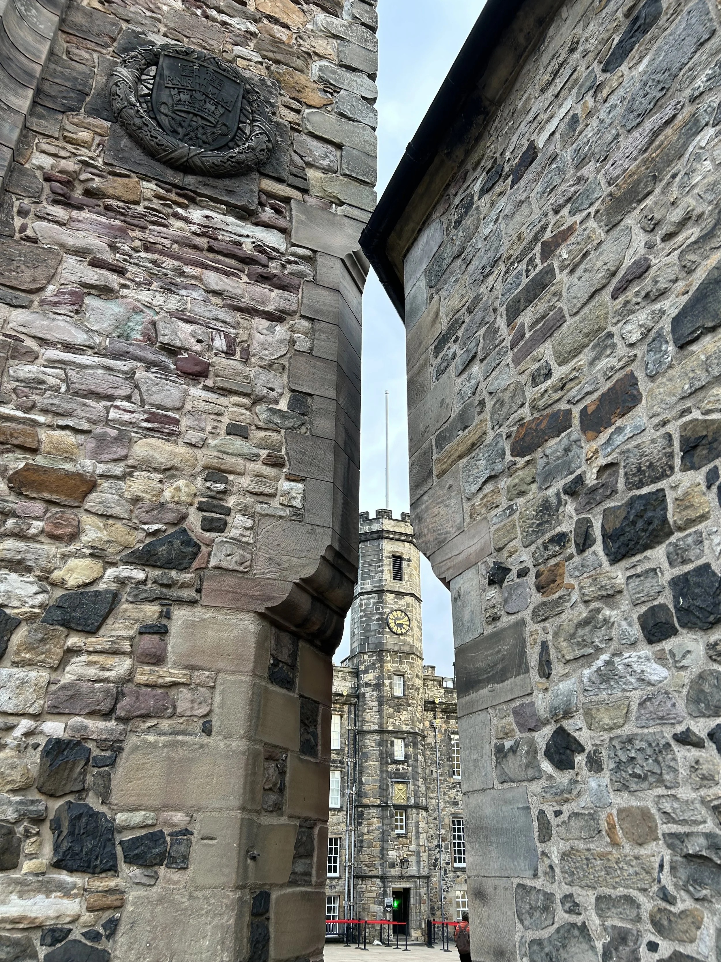 View of a stone clock tower through an opening between two stone walls.