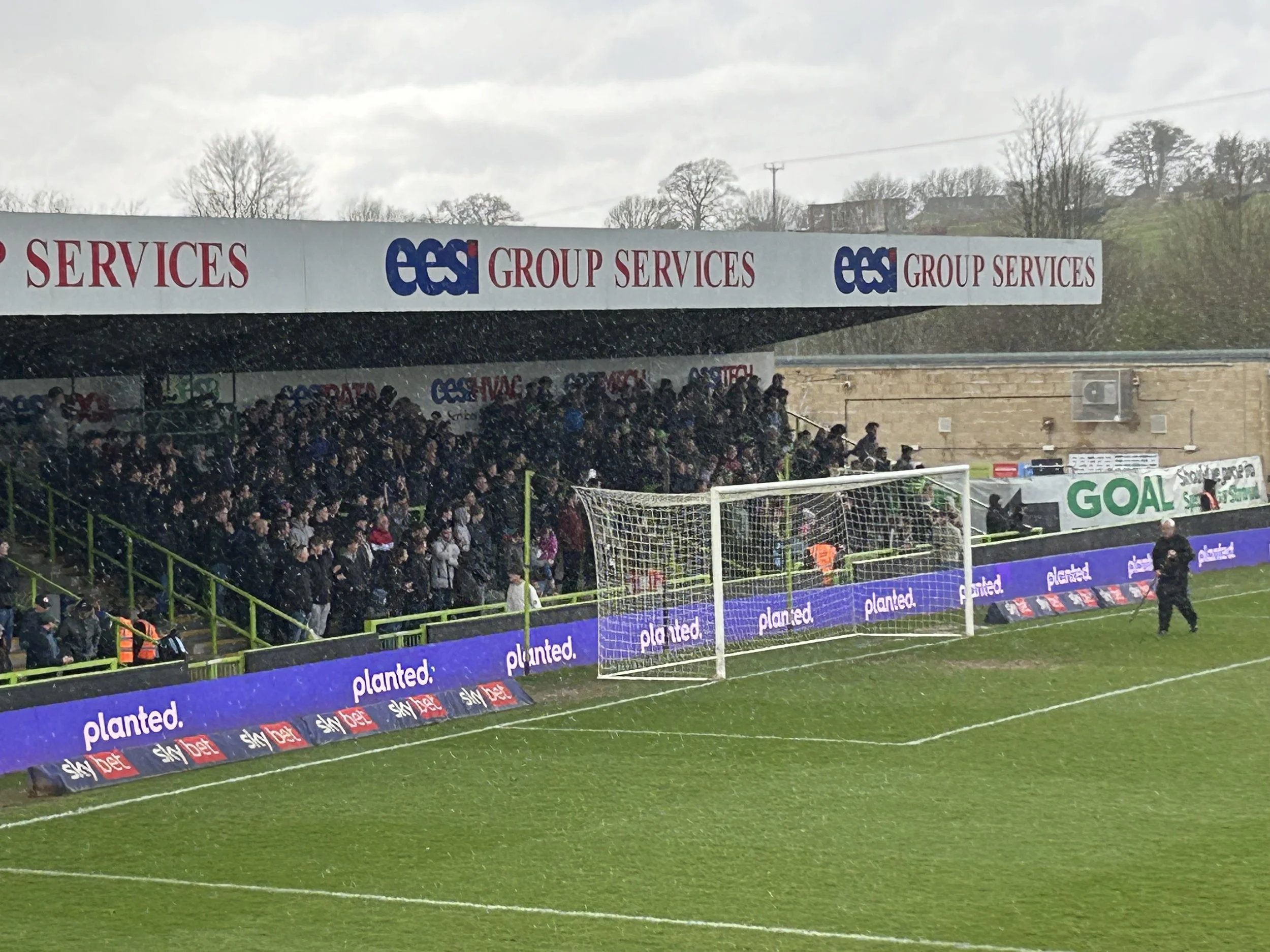 A football stadium with spectators in the stands and a goal on the field, overcast weather.