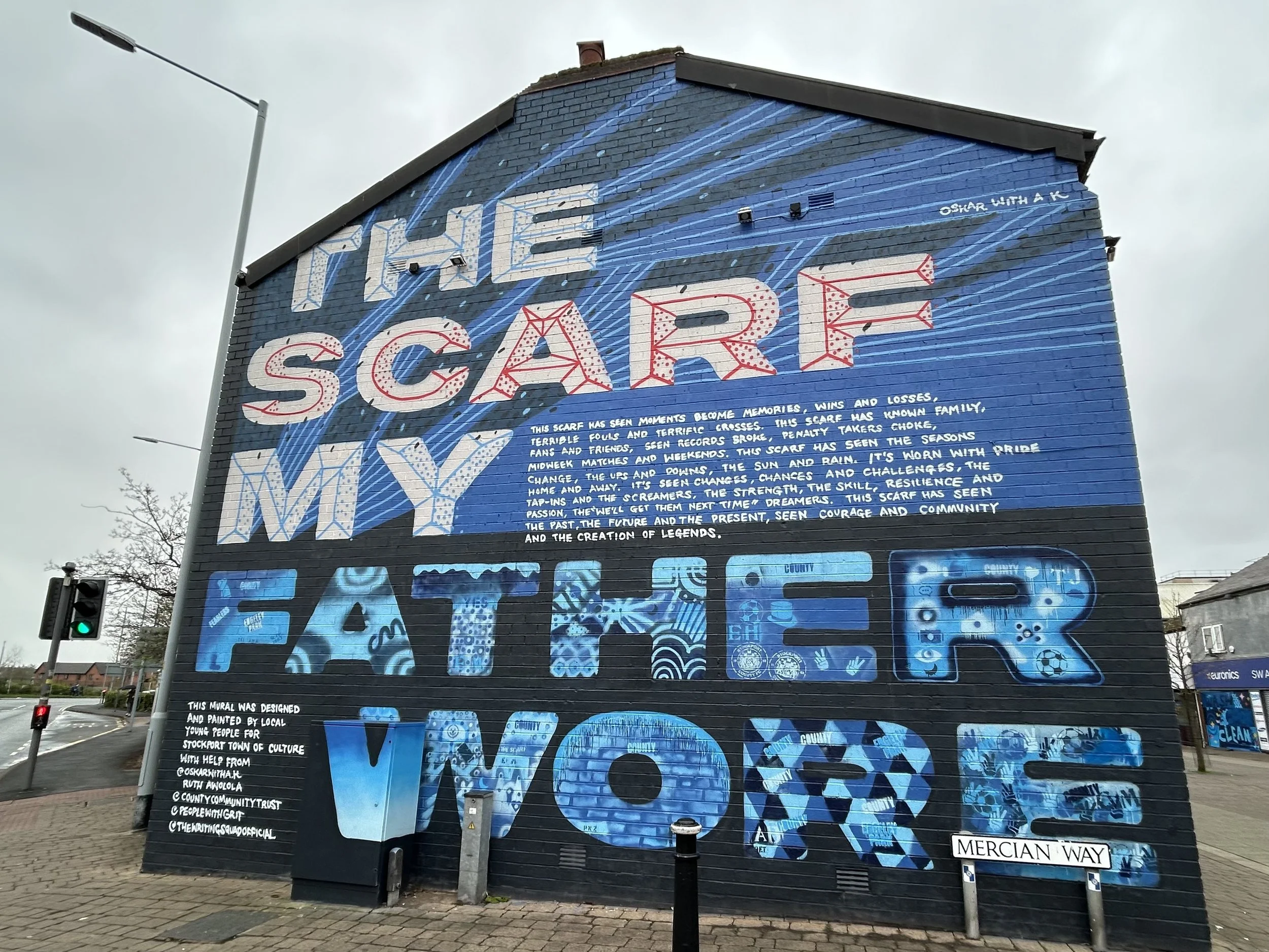 A mural on a brick building features the words "THE SCARF MIRROR" and "FATHER WARD" with detailed text and colorful artistic designs.