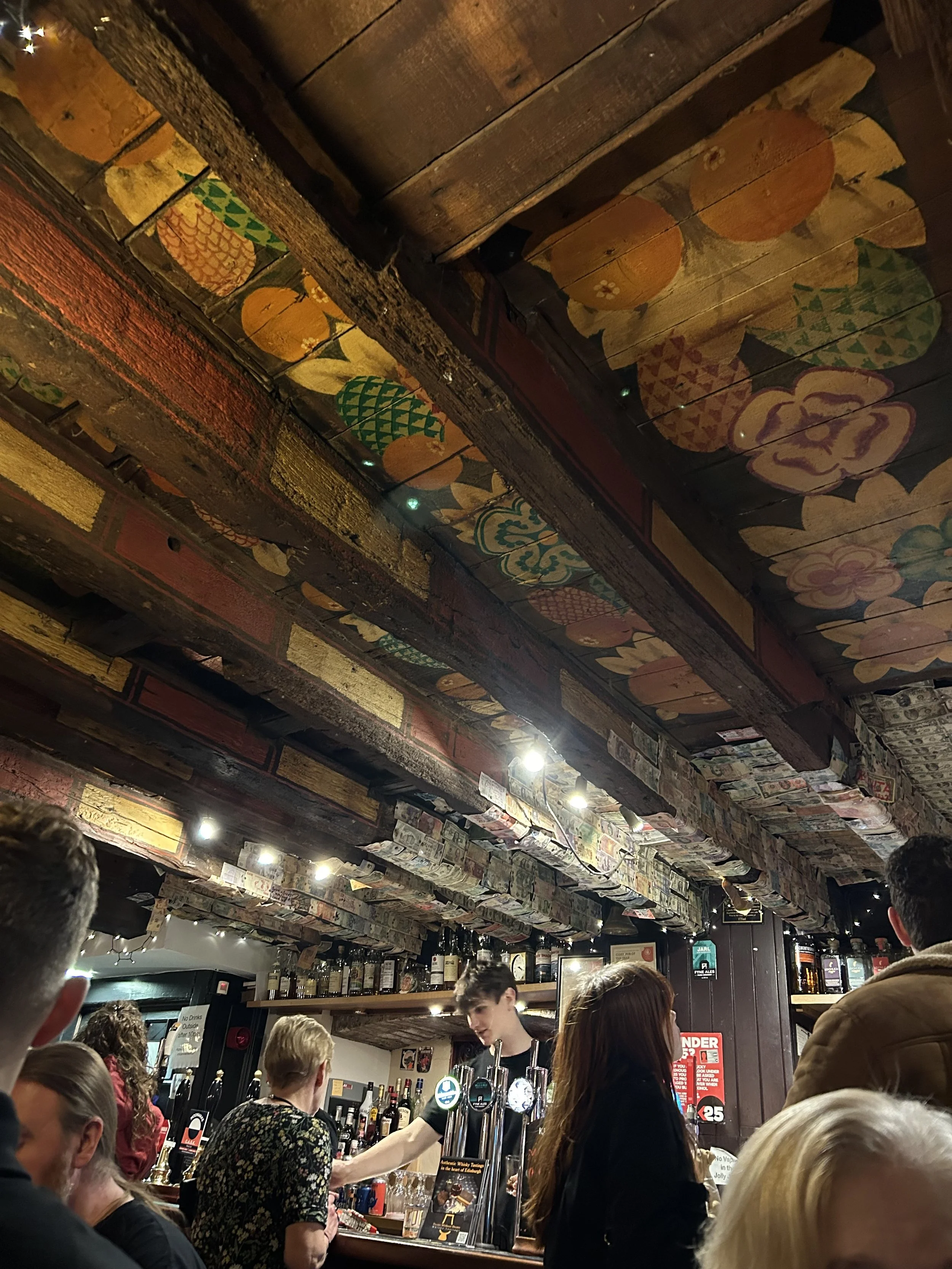 People at bar in a cozy pub with decorated ceiling featuring colorful painted wooden planks.