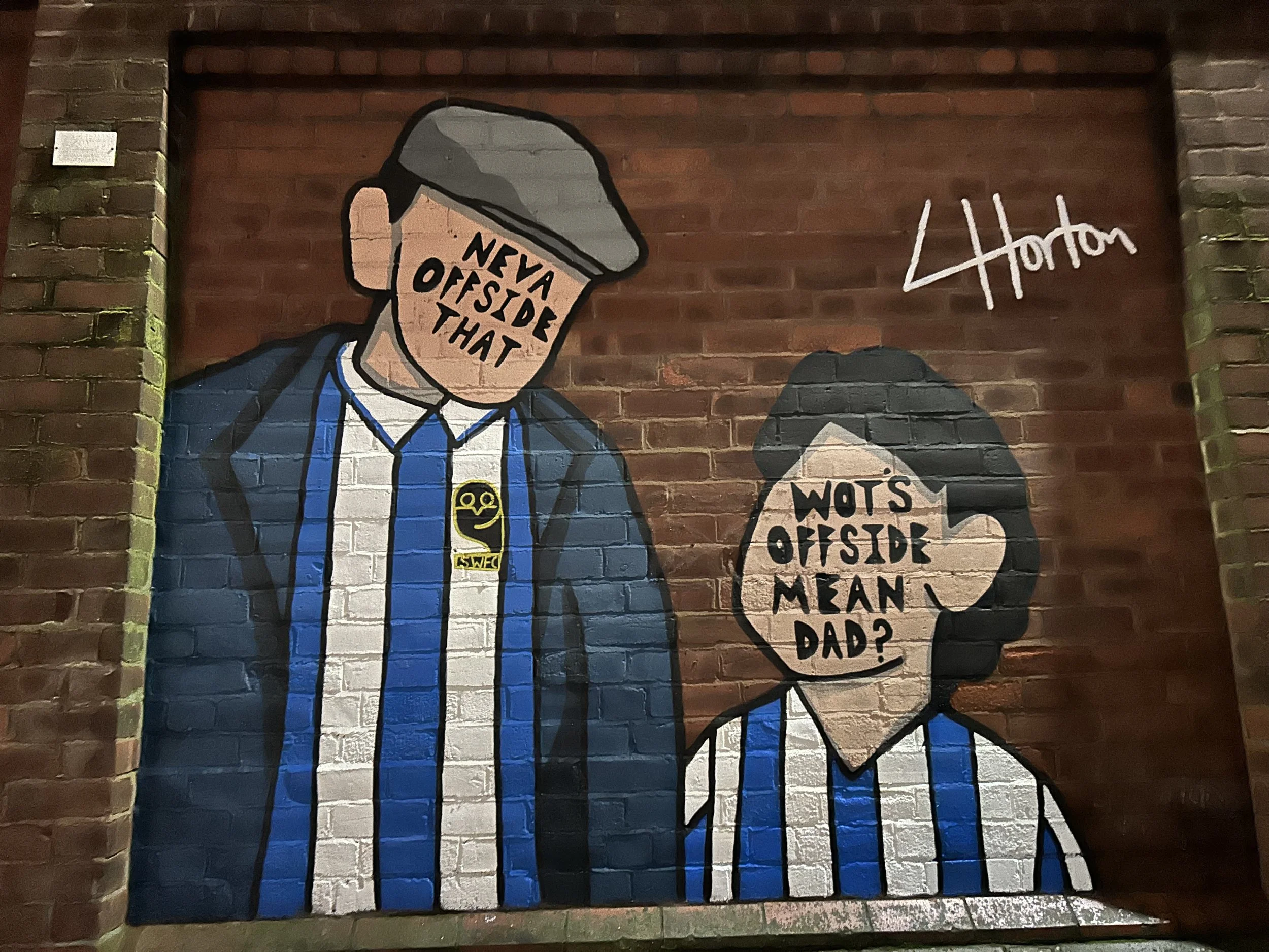 Street art mural of two cartoon characters with speech bubbles. The character on the left has a rectangle-shaped face with the words "NEYA OUTSIDE THAT" on his face, wearing a blue jacket and a badge. The character on the right has an oval face with 
