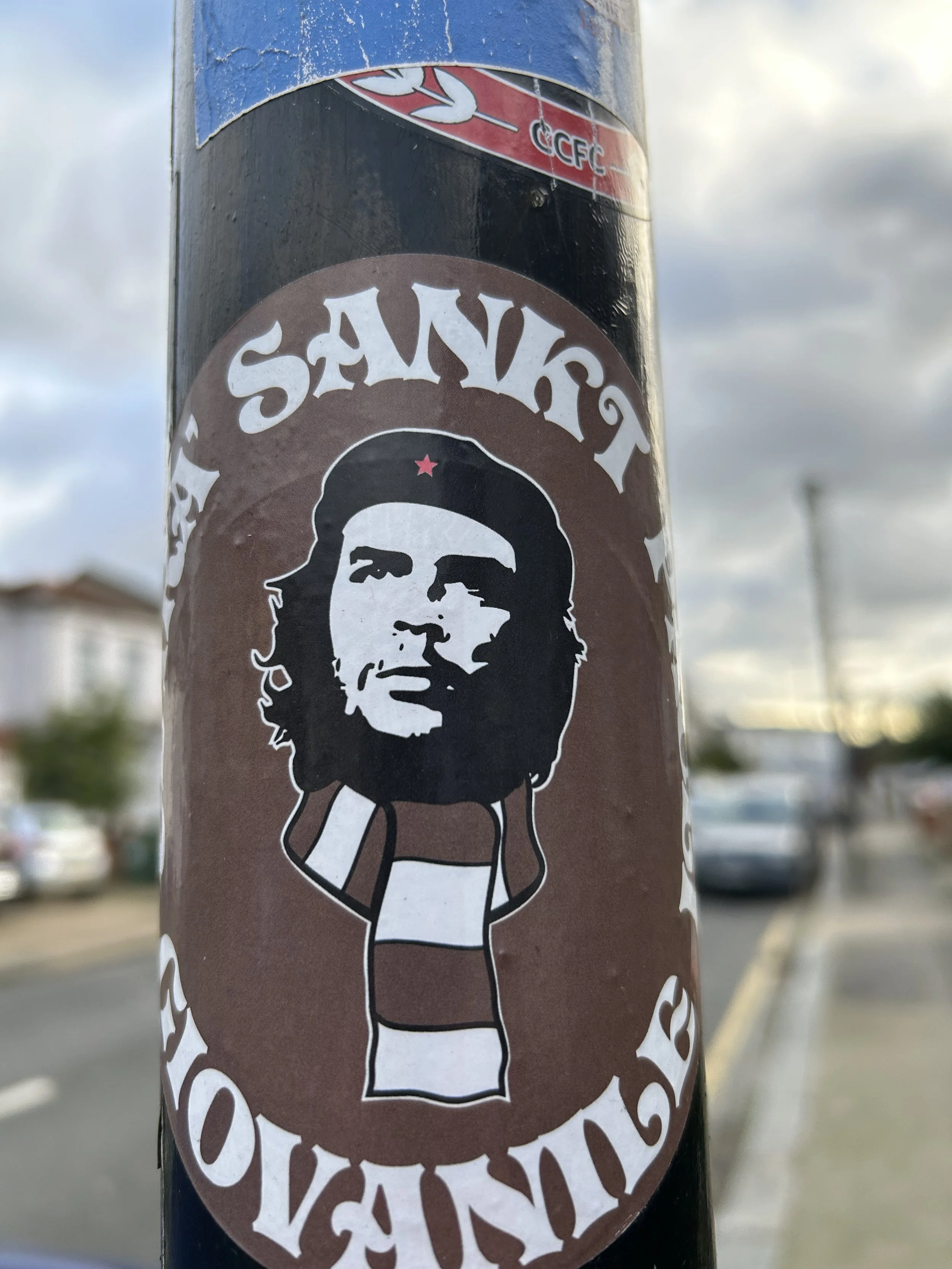 Sticker of Che Guevara with long hair and beard, wearing a striped shirt, and the words "Salvador Revolution" around the image.