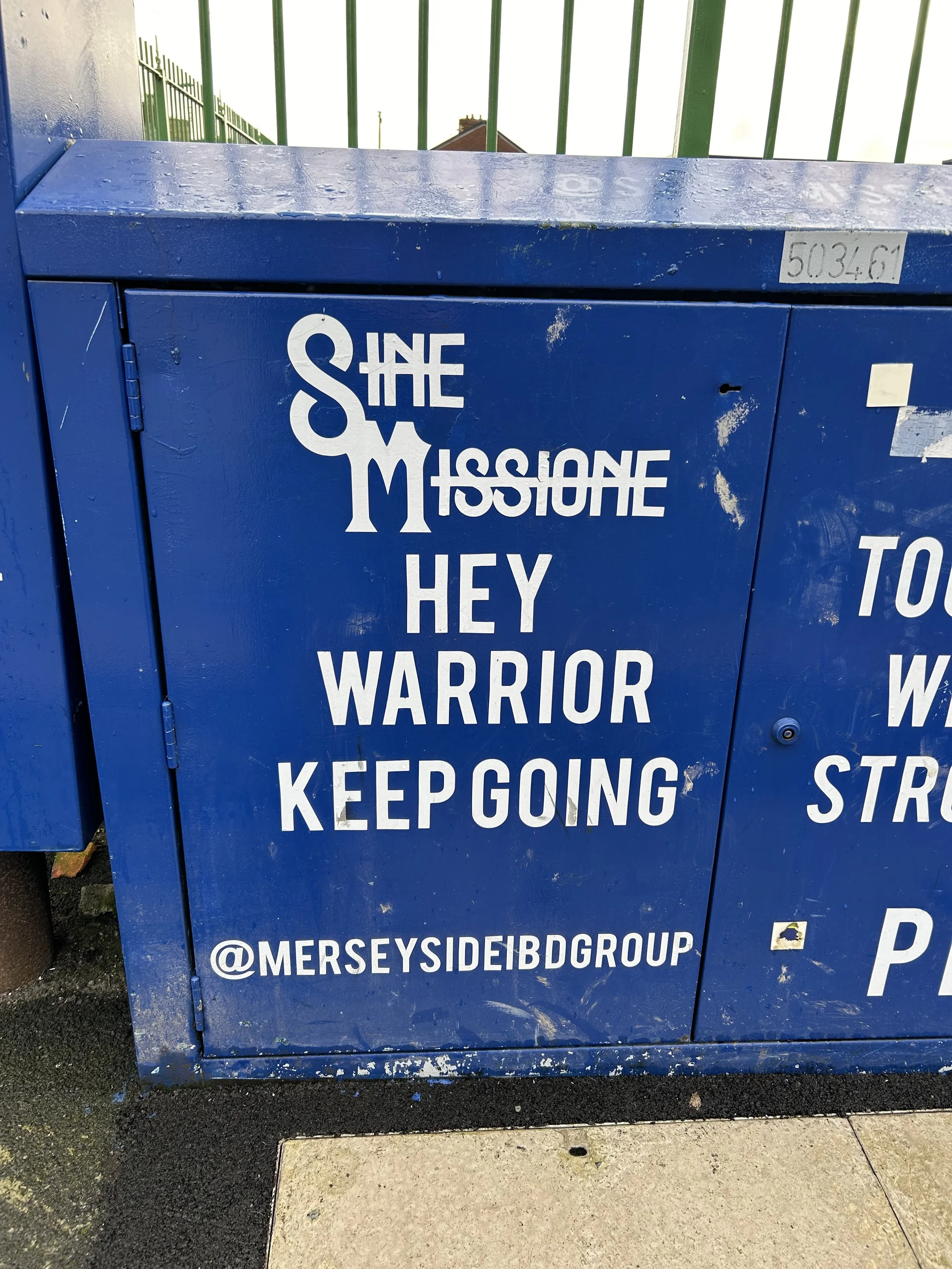 Blue electrical box with white text that reads 'The Missionne Hey Warrior Keep Going' and an Instagram handle '@merseysideibdgrouP'.
