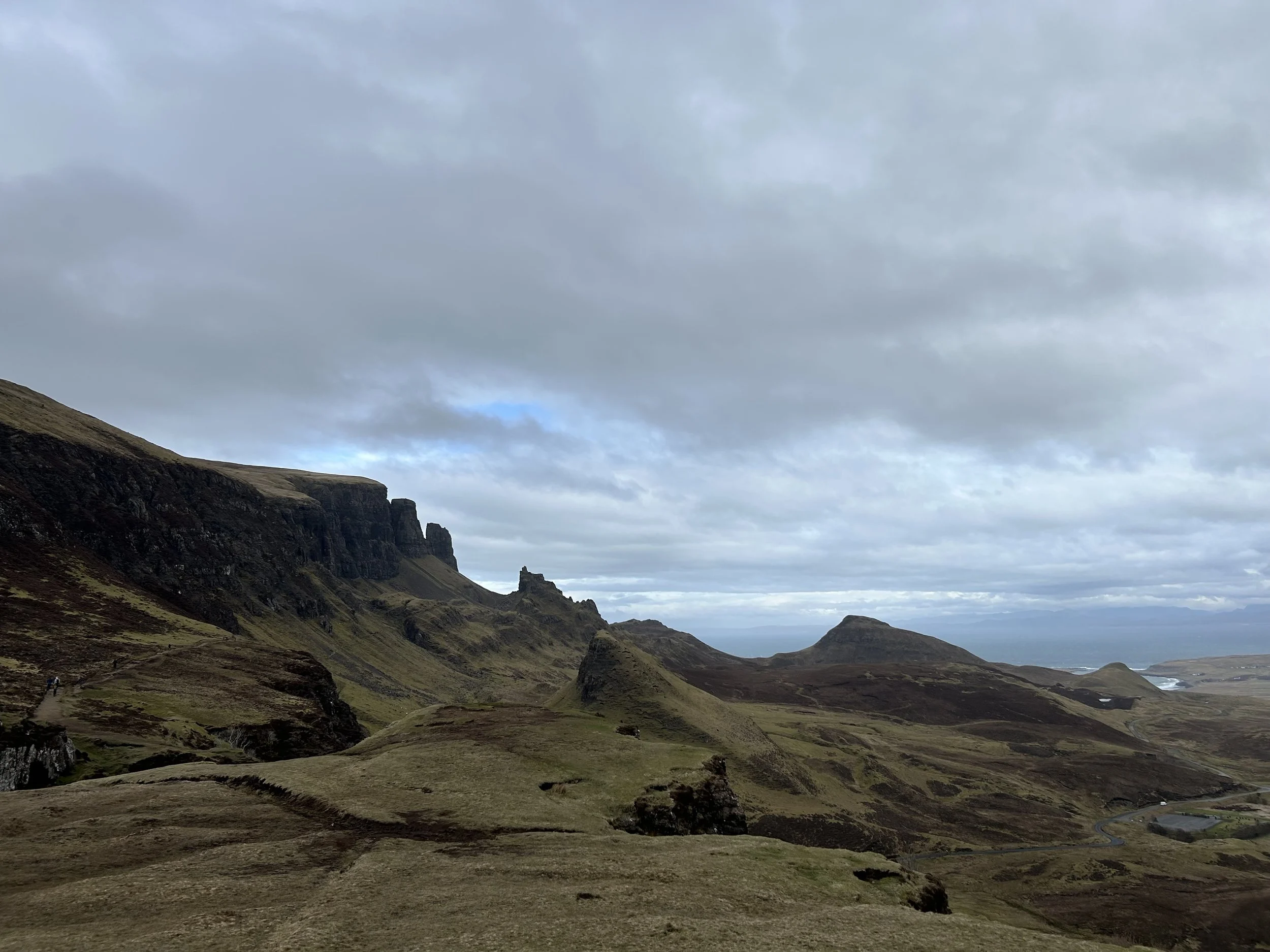 A rugged landscape with rolling green hills, rocky cliffs, and a cloudy sky.