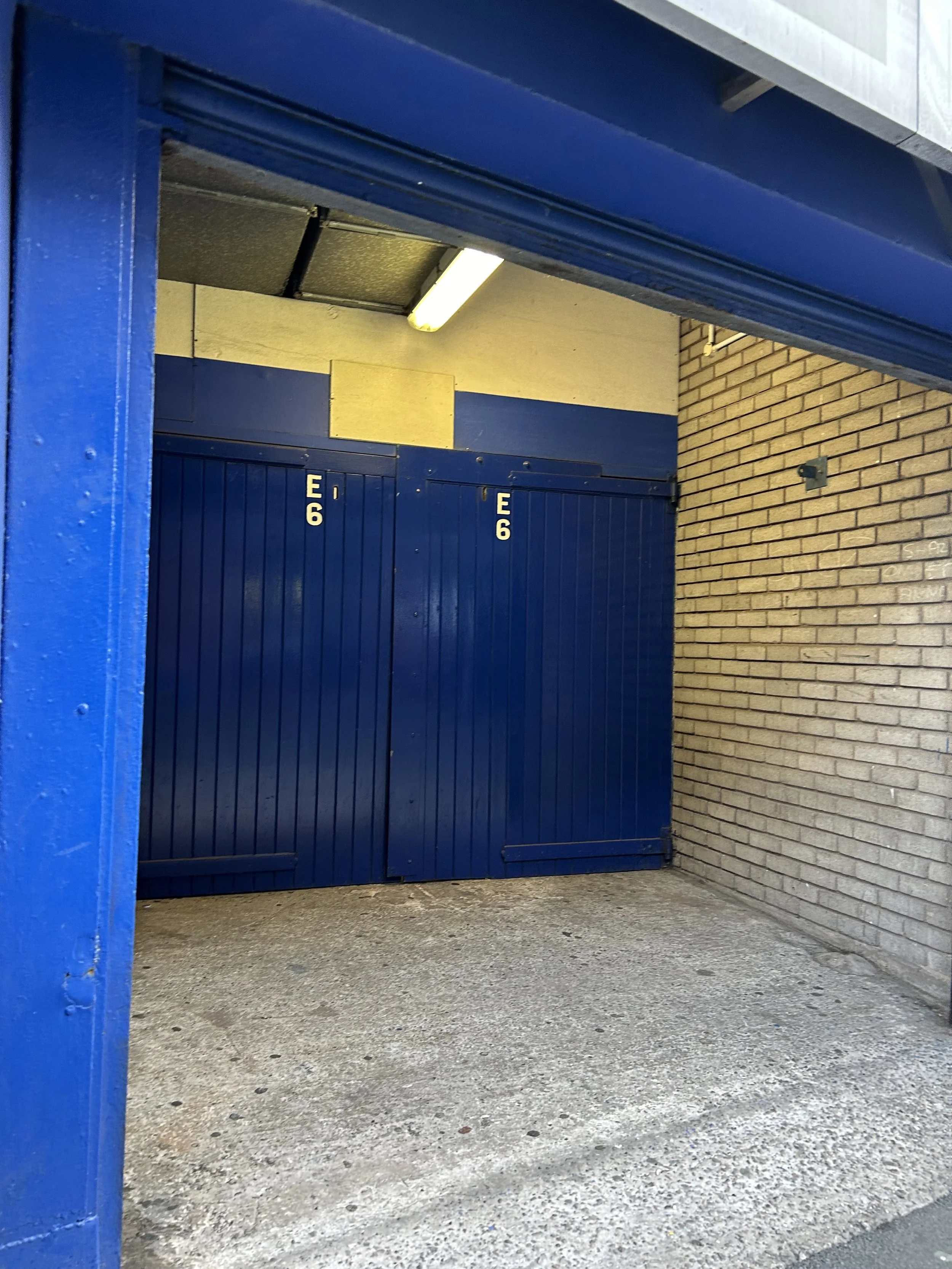 Parking garage entrance with blue metal gates and brick wall on the right.