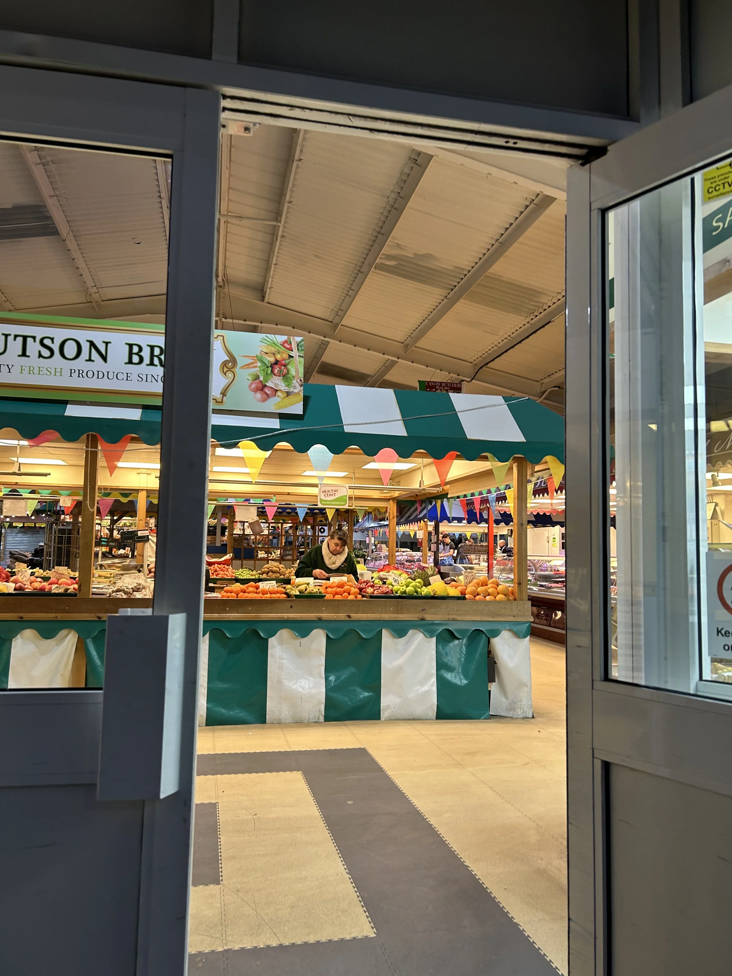 View of a farmers market stall with various fruits and vegetables, seen through an open door.