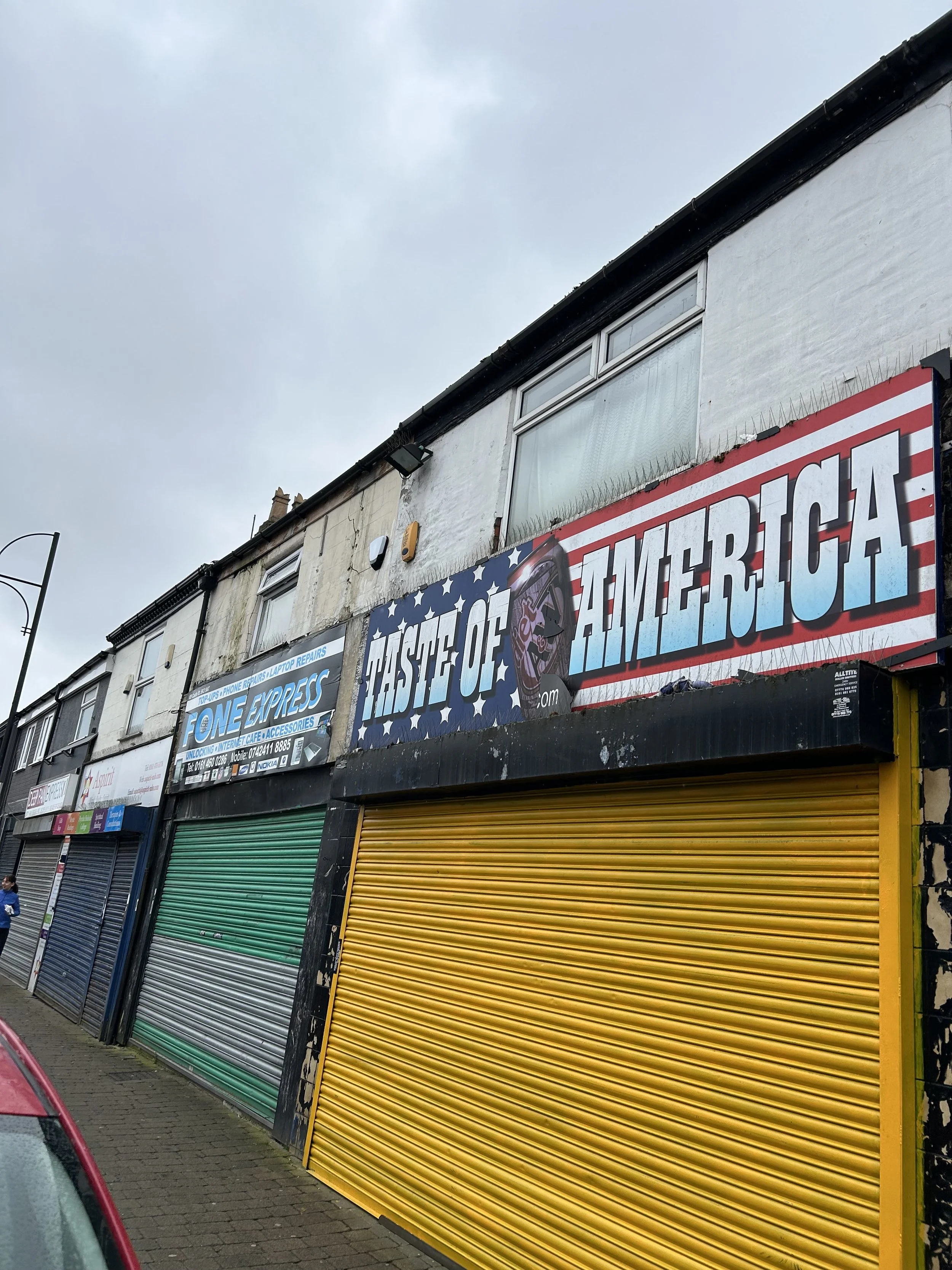 Closed storefront with colorful rolling shutters and a sign that reads 'TASTE OF AMERICA' with an American flag background.