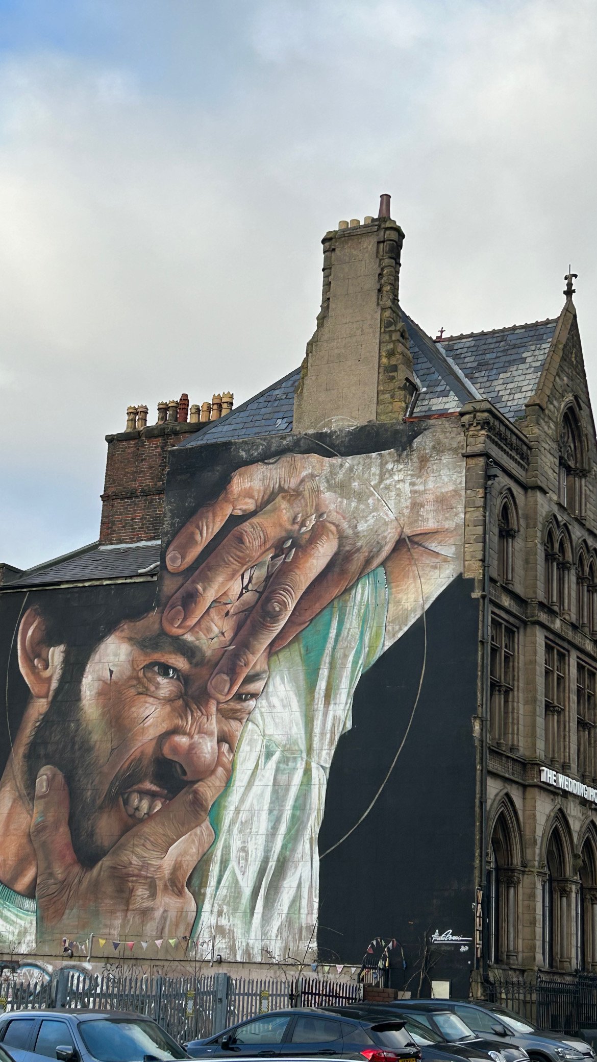 A large mural of a man with a pained expression, holding his forehead with his right hand, painted on the side of a building.