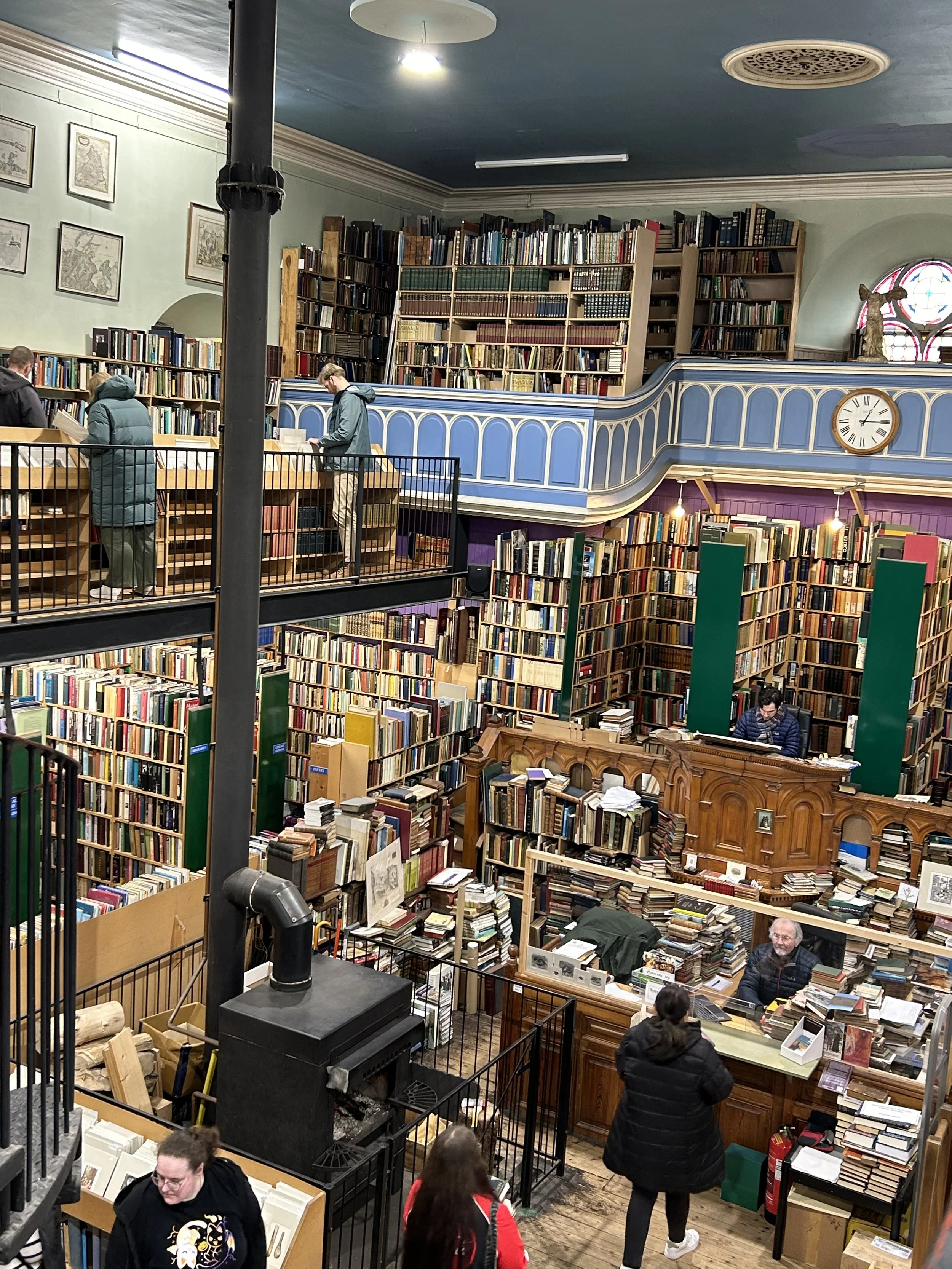 Multiple levels filled with books and people browsing the shelves, inside a large, historic bookstore with high ceilings and decorative architecture.