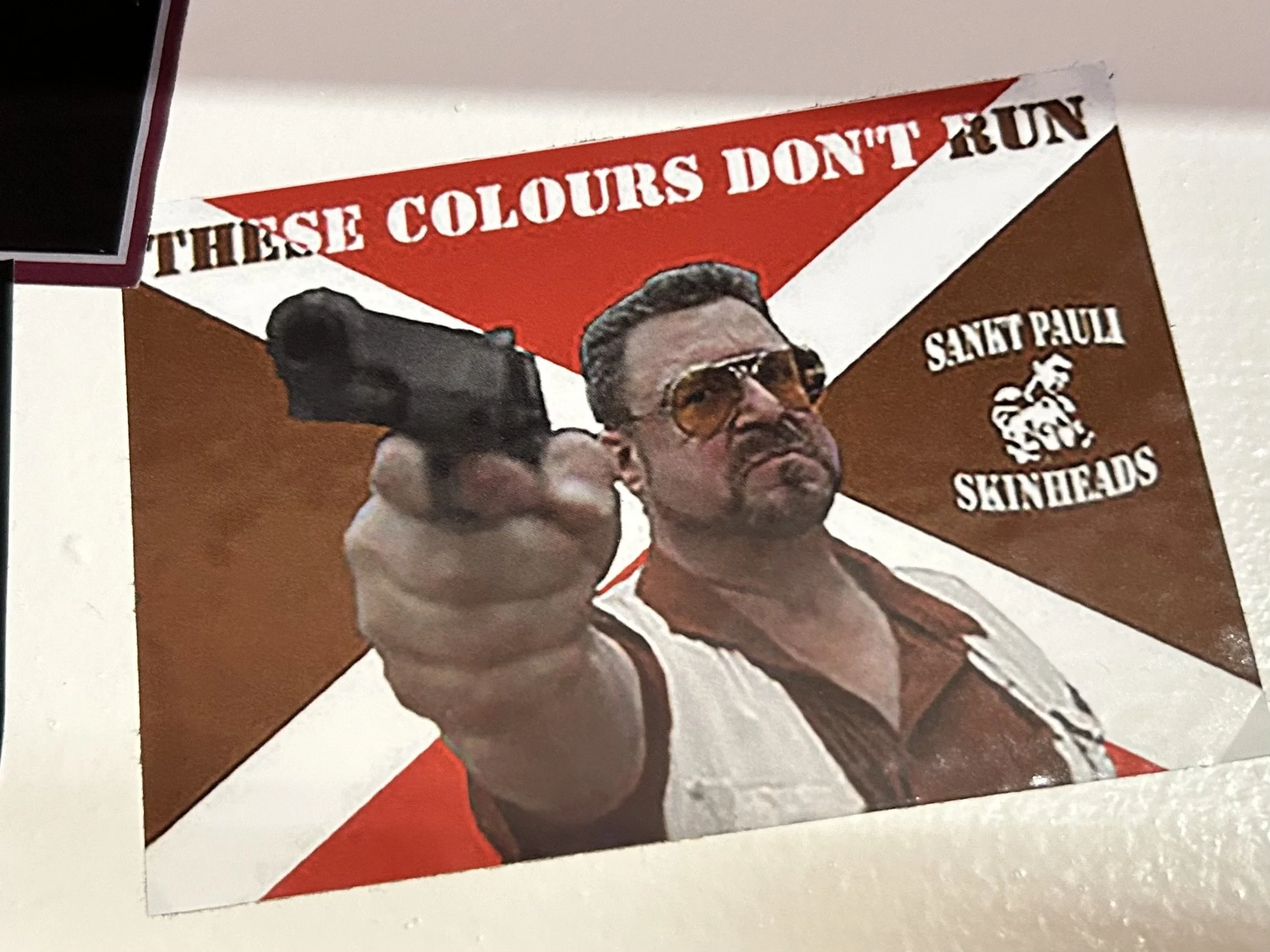 Poster featuring a man with sunglasses pointing a gun, with the text "These colours don't run" and mentions of Saint Pauli skinheads.