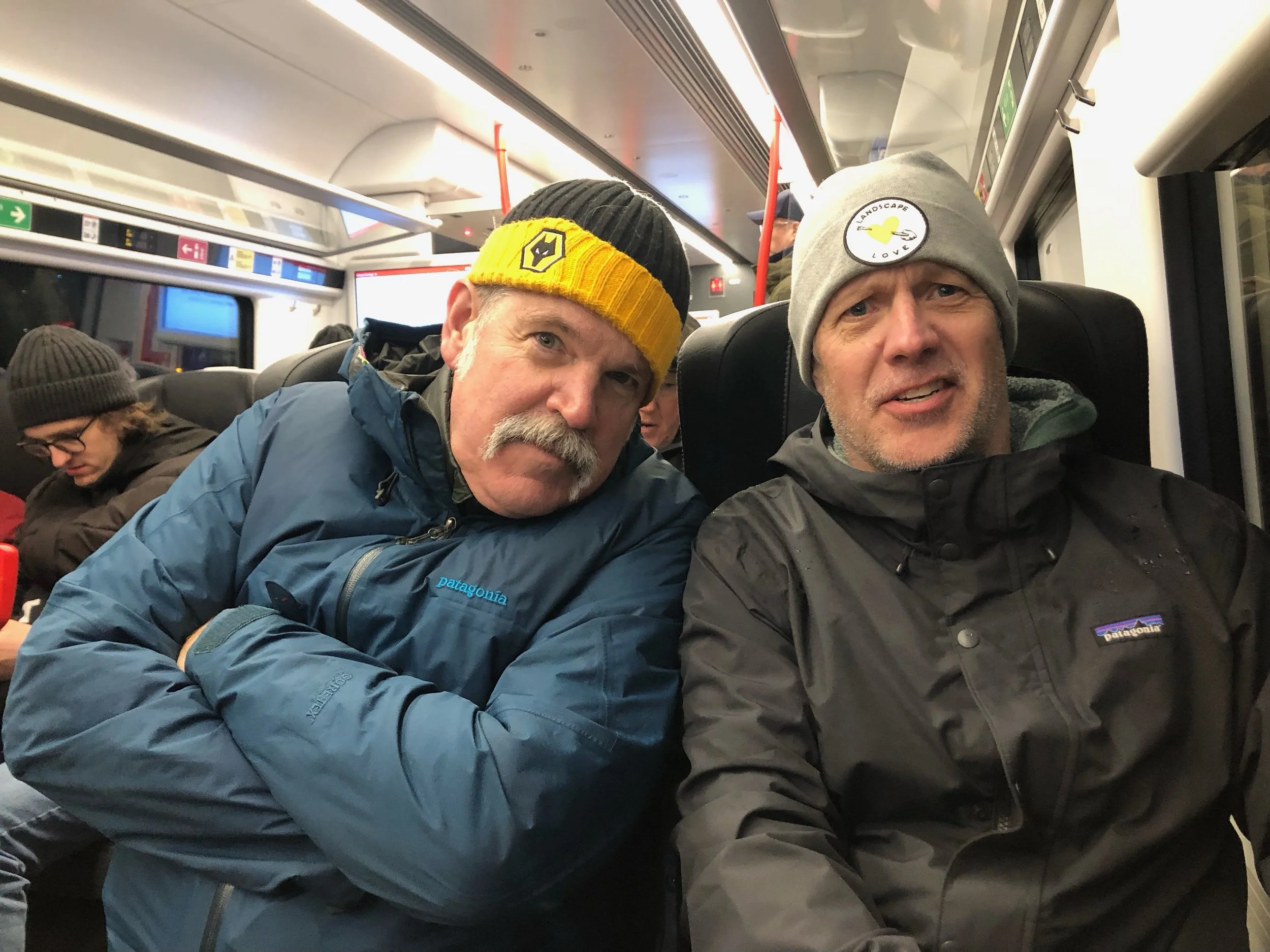 Two men wearing beanies and Patagonia jackets sitting on a bus.