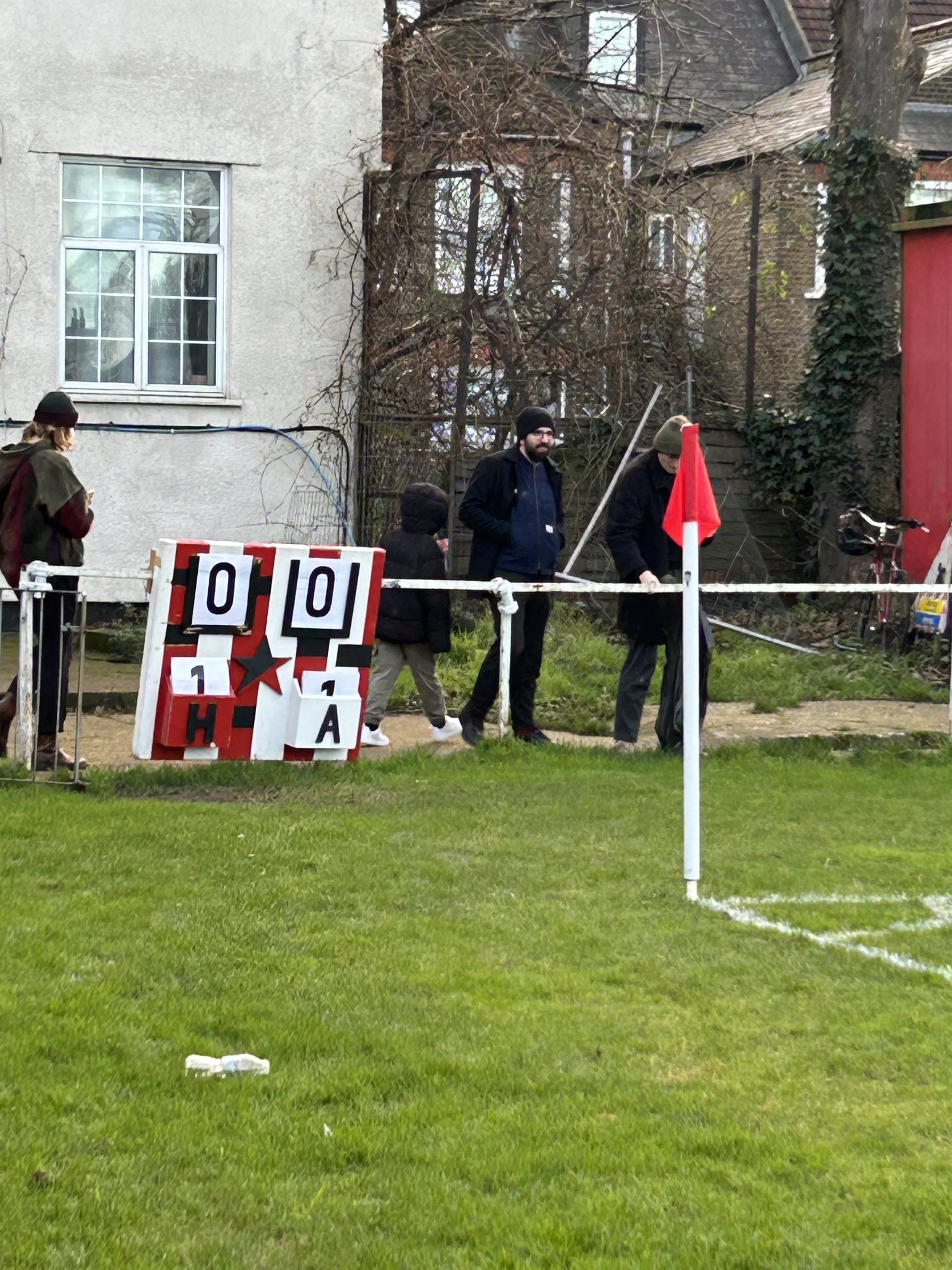 People walking near a sign with score numbers, trees, and residential buildings in the background.