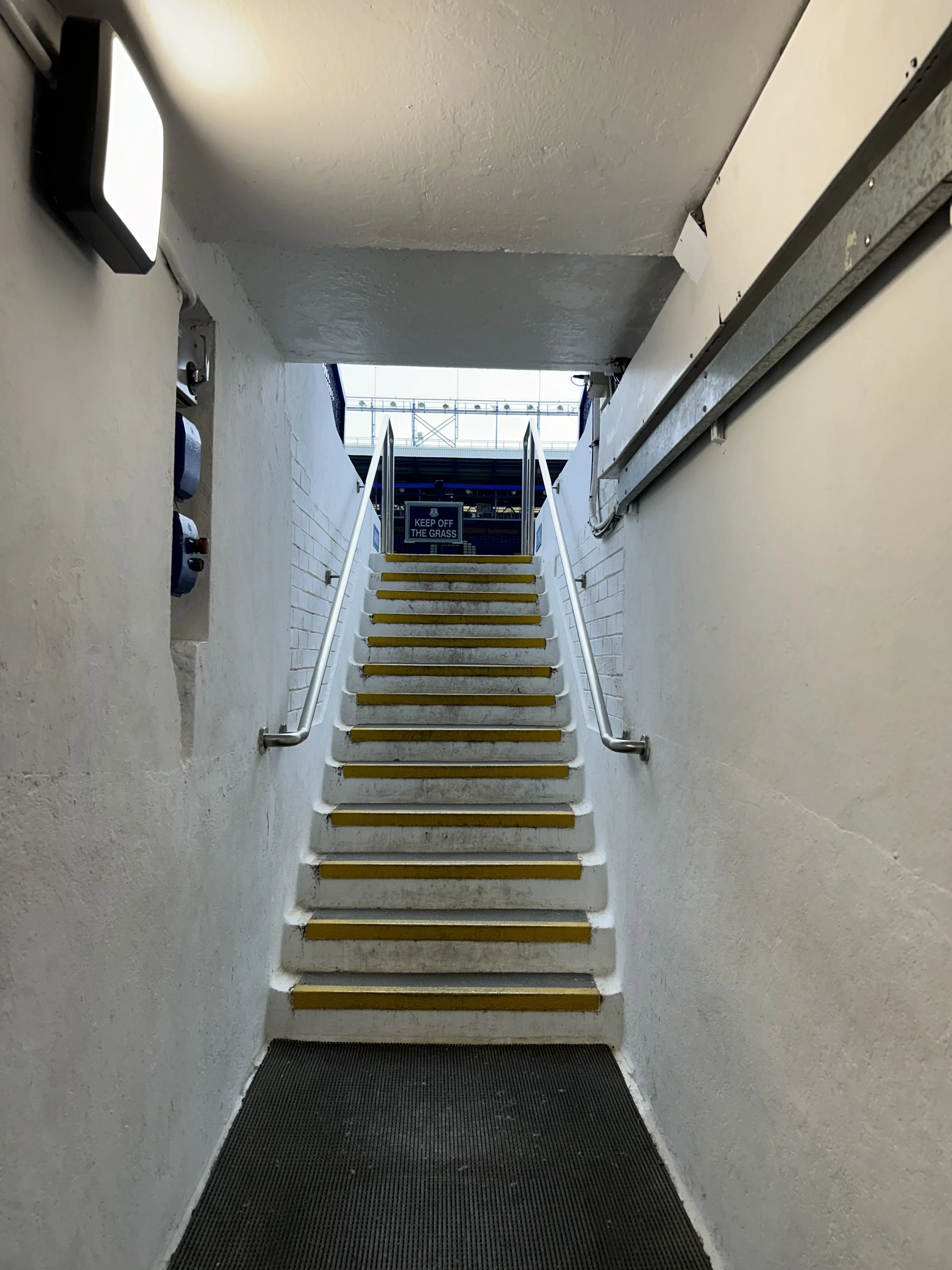 Staircase with yellow safety strips, metal handrails leading up to a platform at a train station, with a 