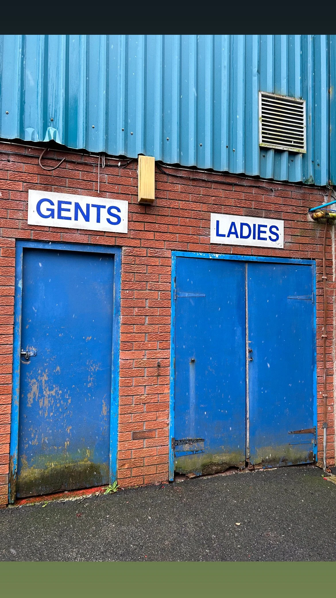 Outside men's and women's restroom doors with signs labeled 'GENTS' and 'LADIES' on a red brick building with blue doors.