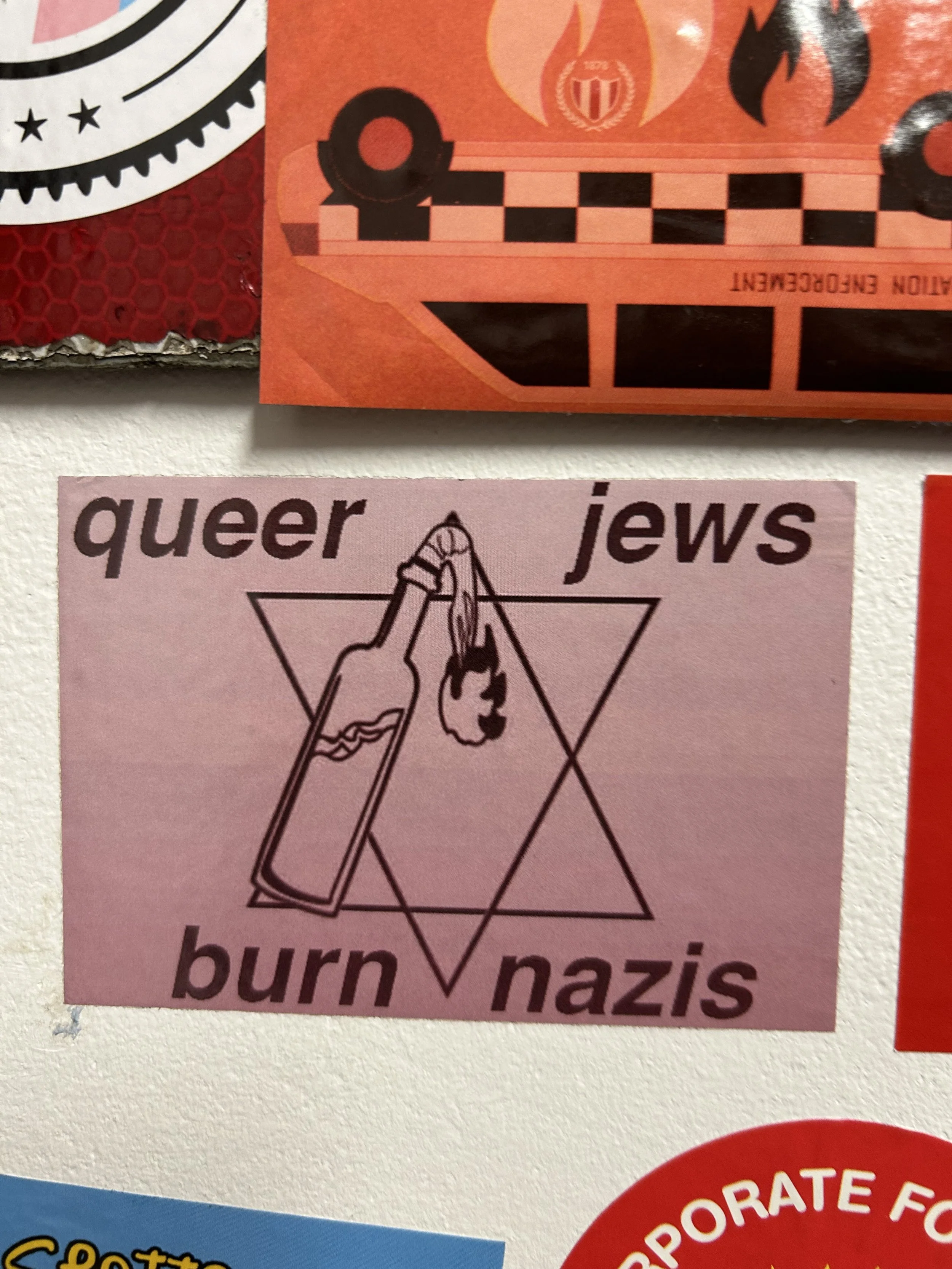 Pink sticker with an illustration of a bottle with a drop of liquid, surrounded by a triangle and lines, with words surrounding it saying "queer," "jews," "burn," and "nazis."