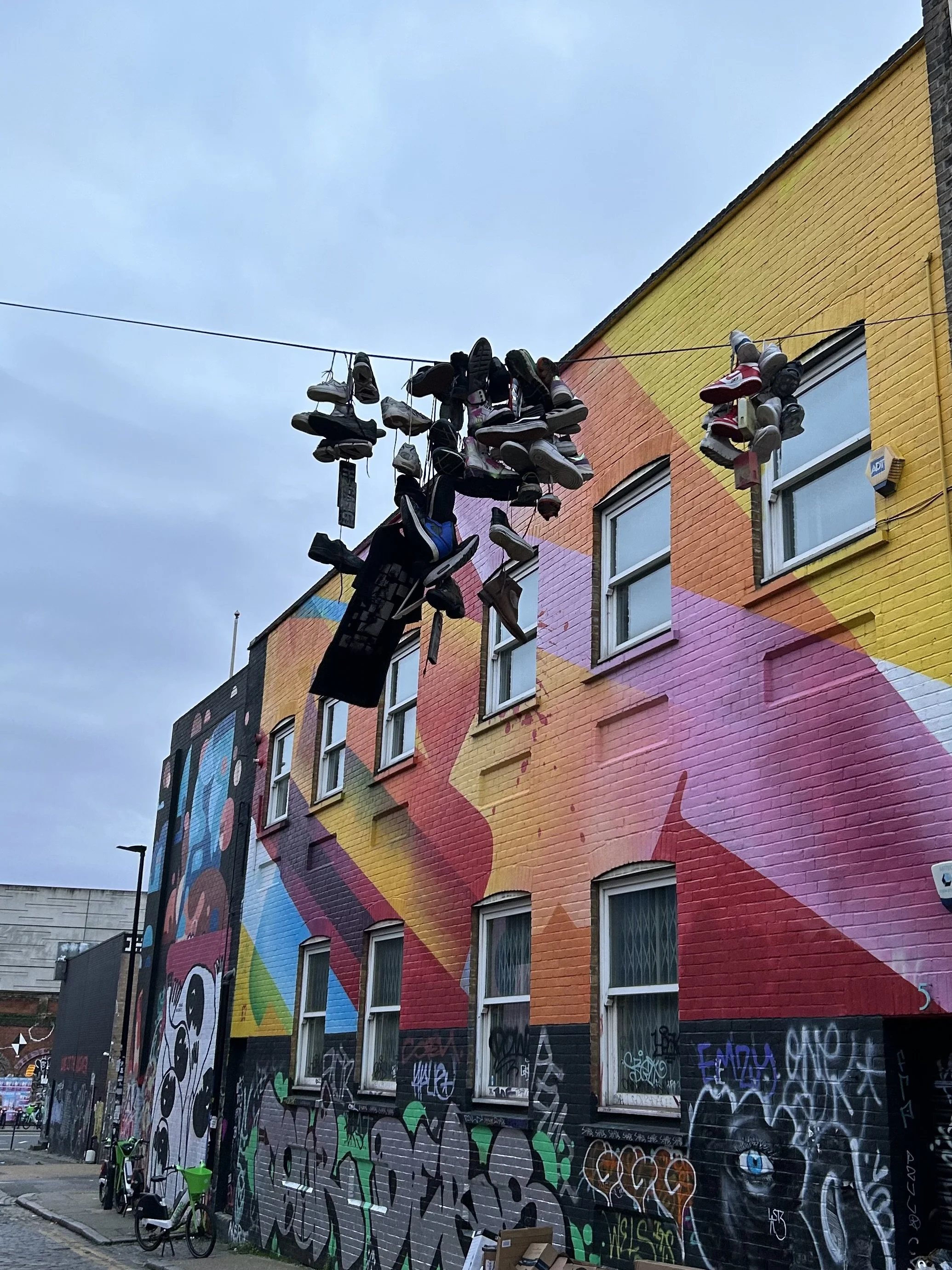 Colorful mural on a building wall with graffiti art, with shoes hanging from a clothesline above.