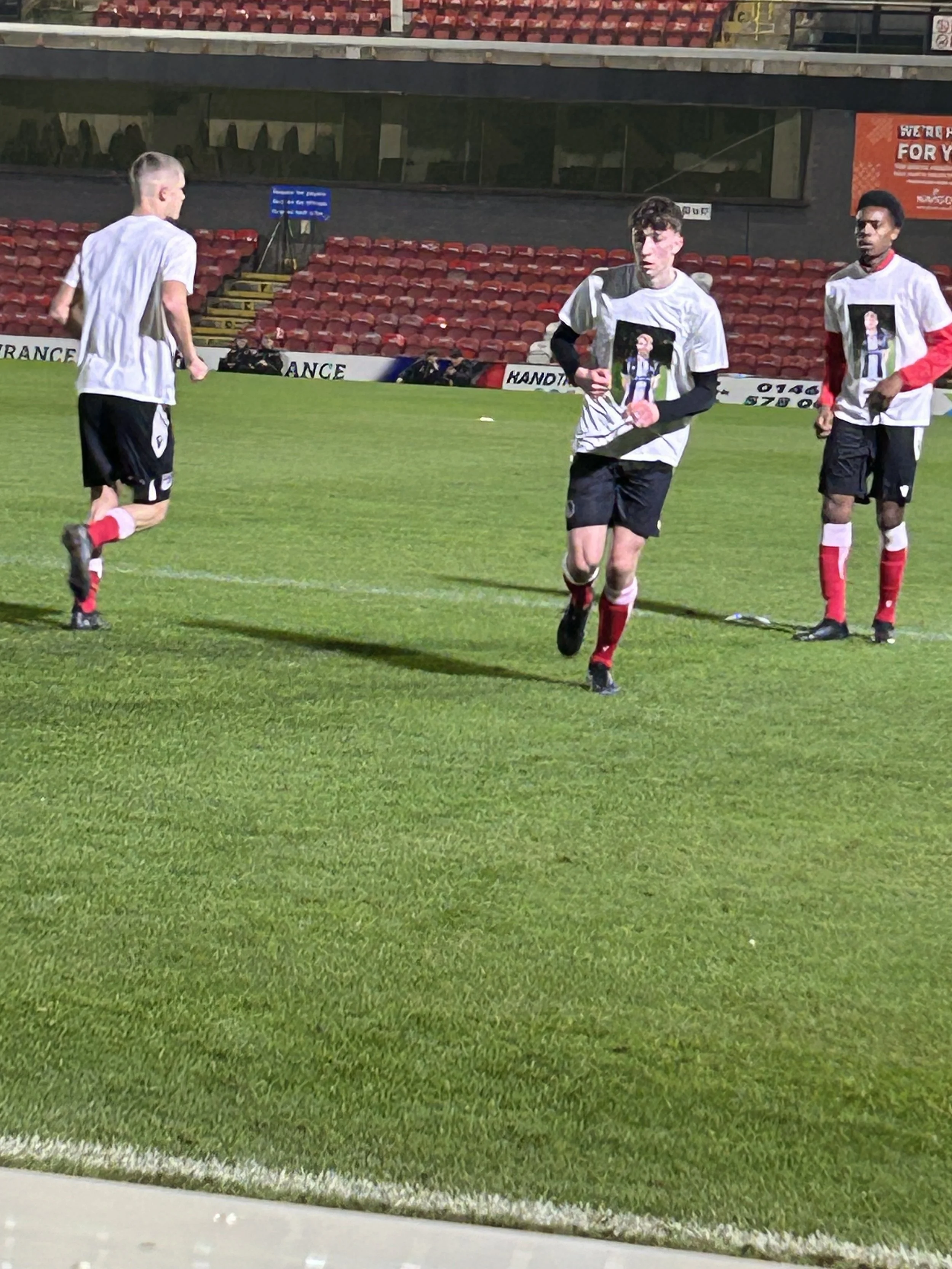 Three soccer players jogging on the field during a game or practice, wearing gray and black uniforms with red socks.