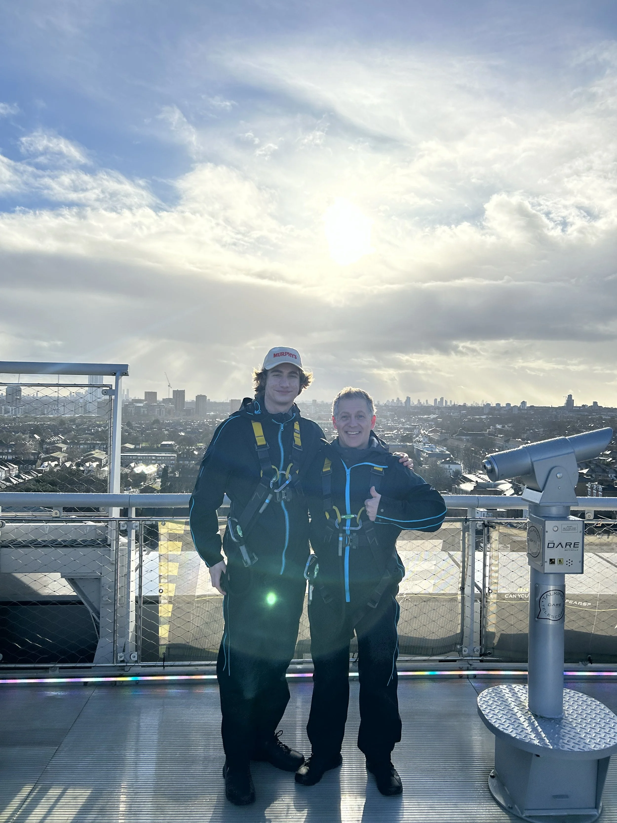 Author Todd Smith and son, in winter clothing on an outdoor observation deck with a cityscape in the background and the sun shining through clouds.