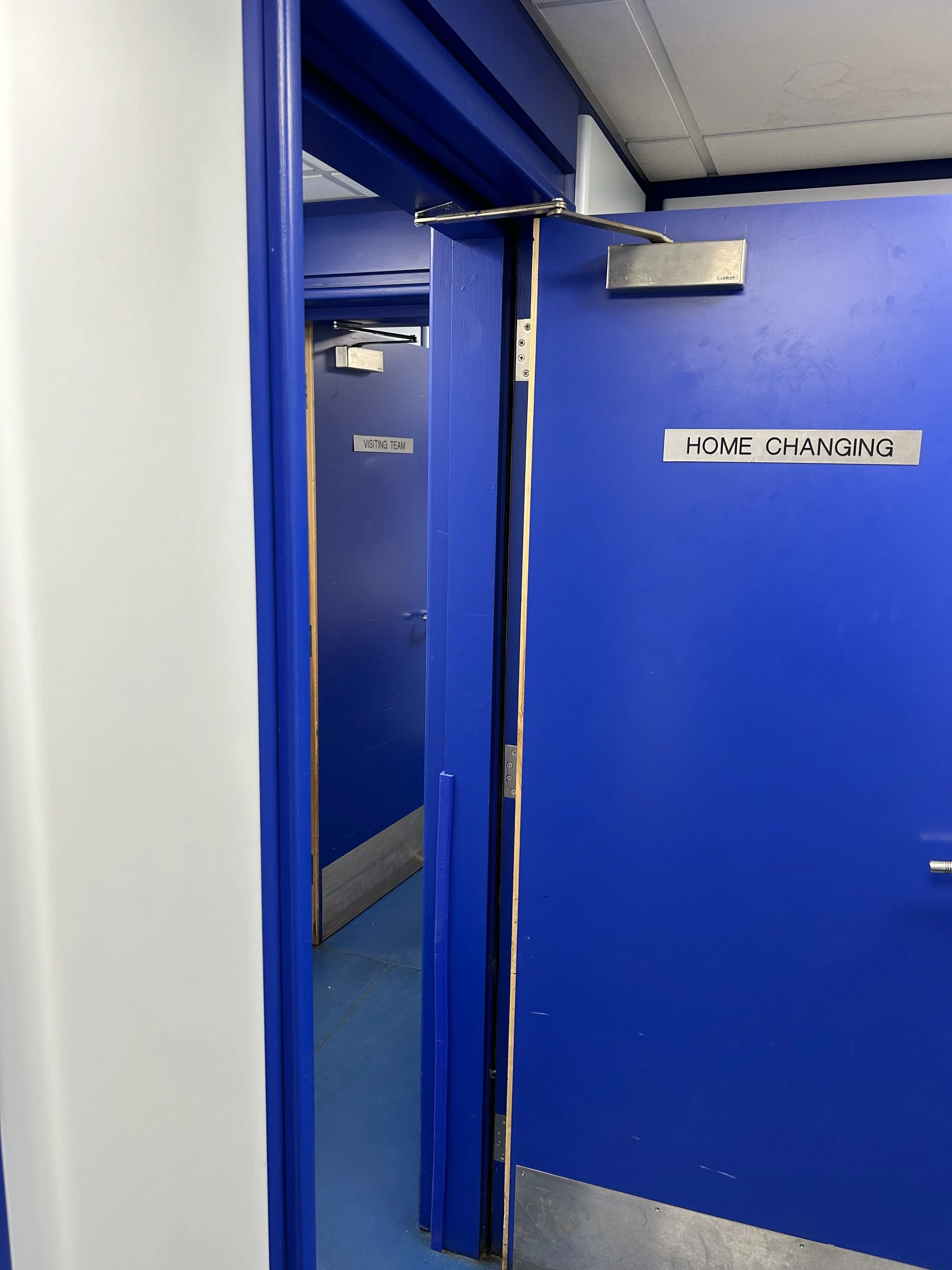 Blue doors labeled 'HOME CHANGING' and 'VISITING TEAM' in a school or recreational facility locker room area.