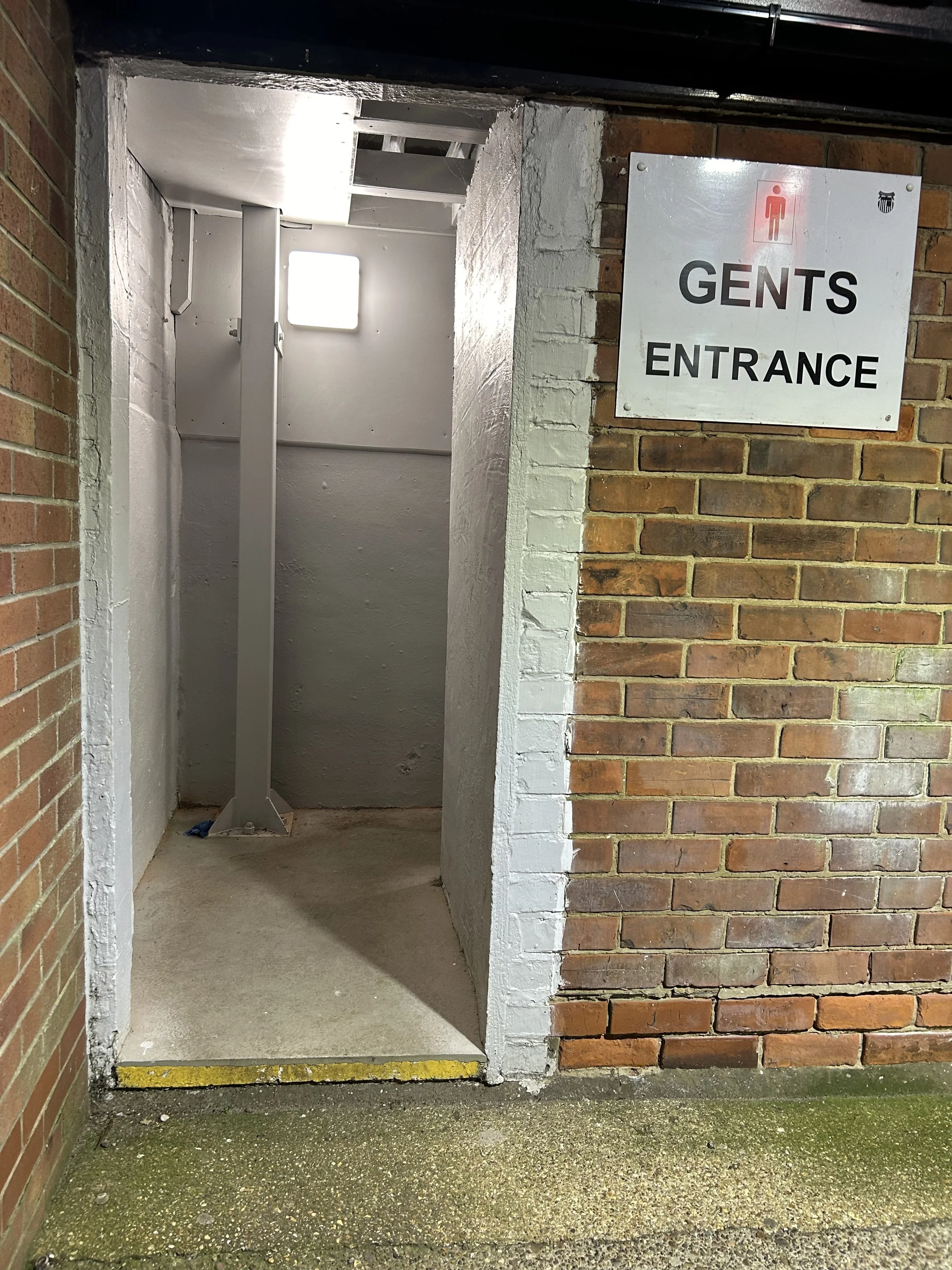 Entrance to men's restroom with sign indicating 'GENTS ENTRANCE' on brick wall.