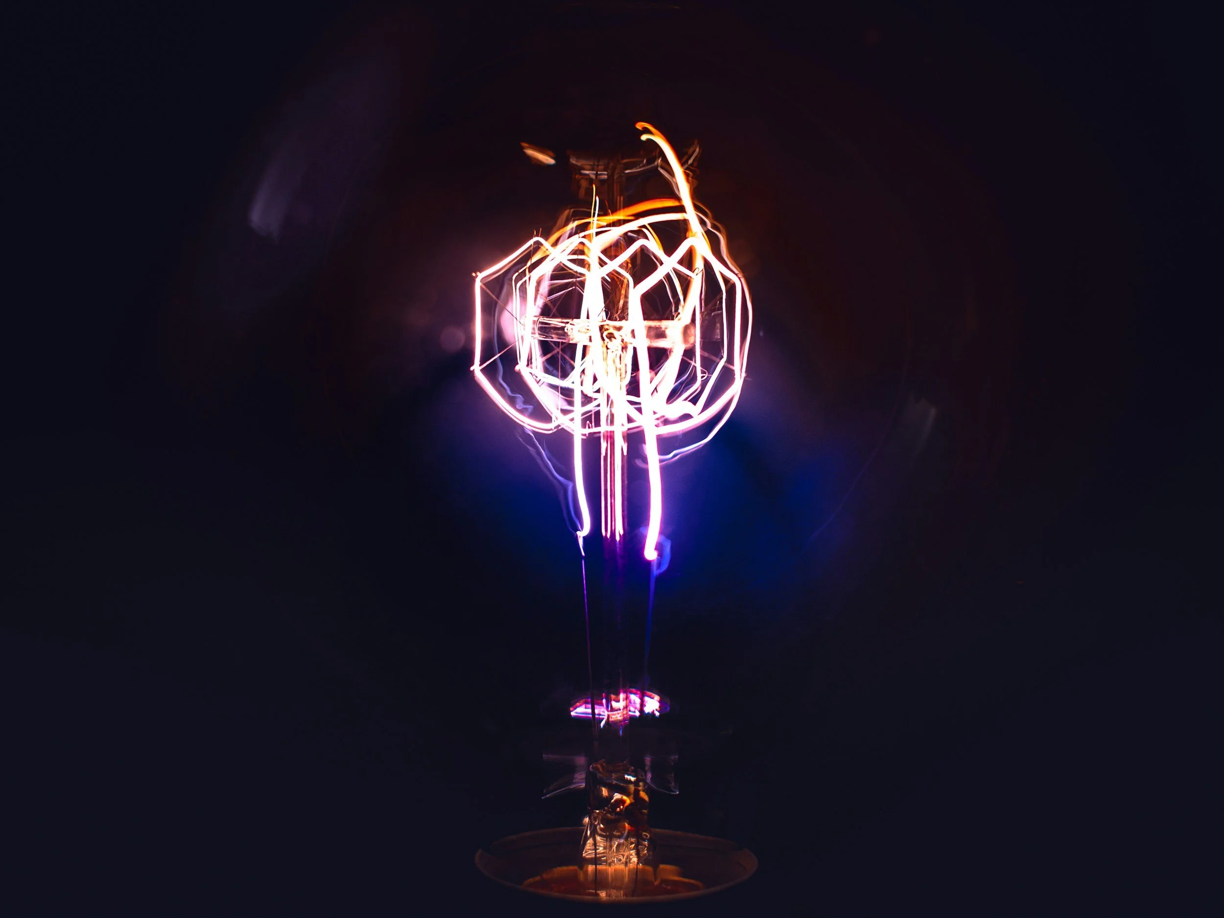 Close-up of a glowing vintage incandescent light bulb filament against a dark background.