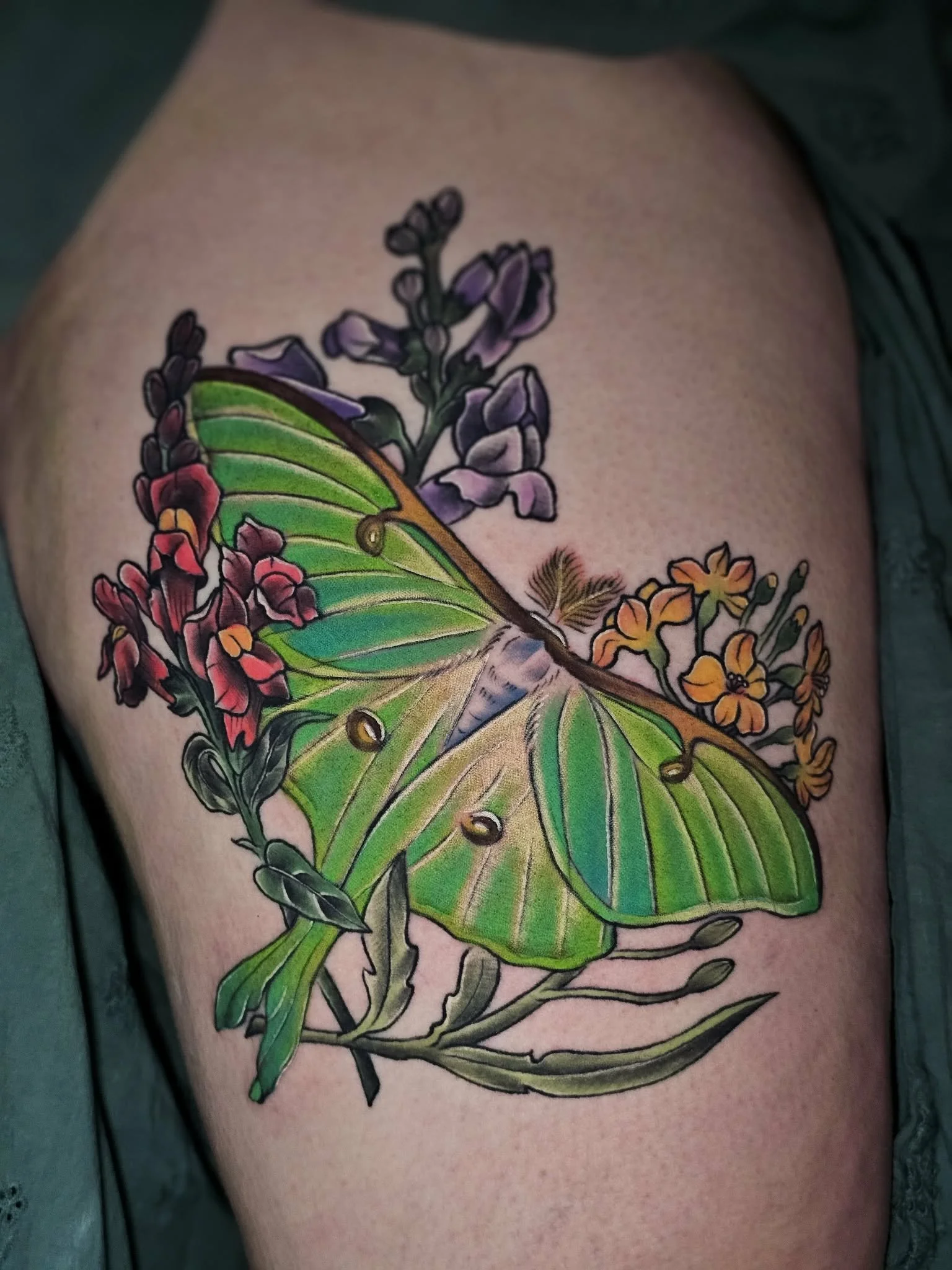 Colorful tattoo of a green and yellow butterfly sitting on purple, pink, and orange flowers.