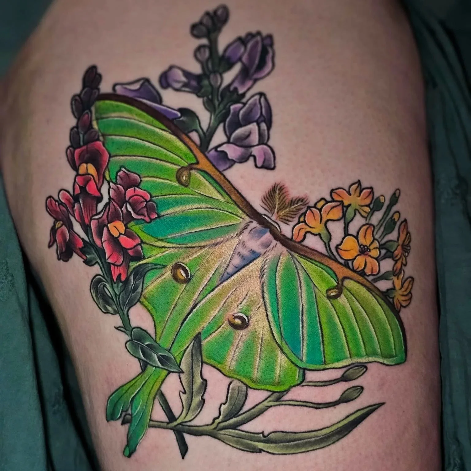 Colorful tattoo of a green butterfly with floral elements on skin.