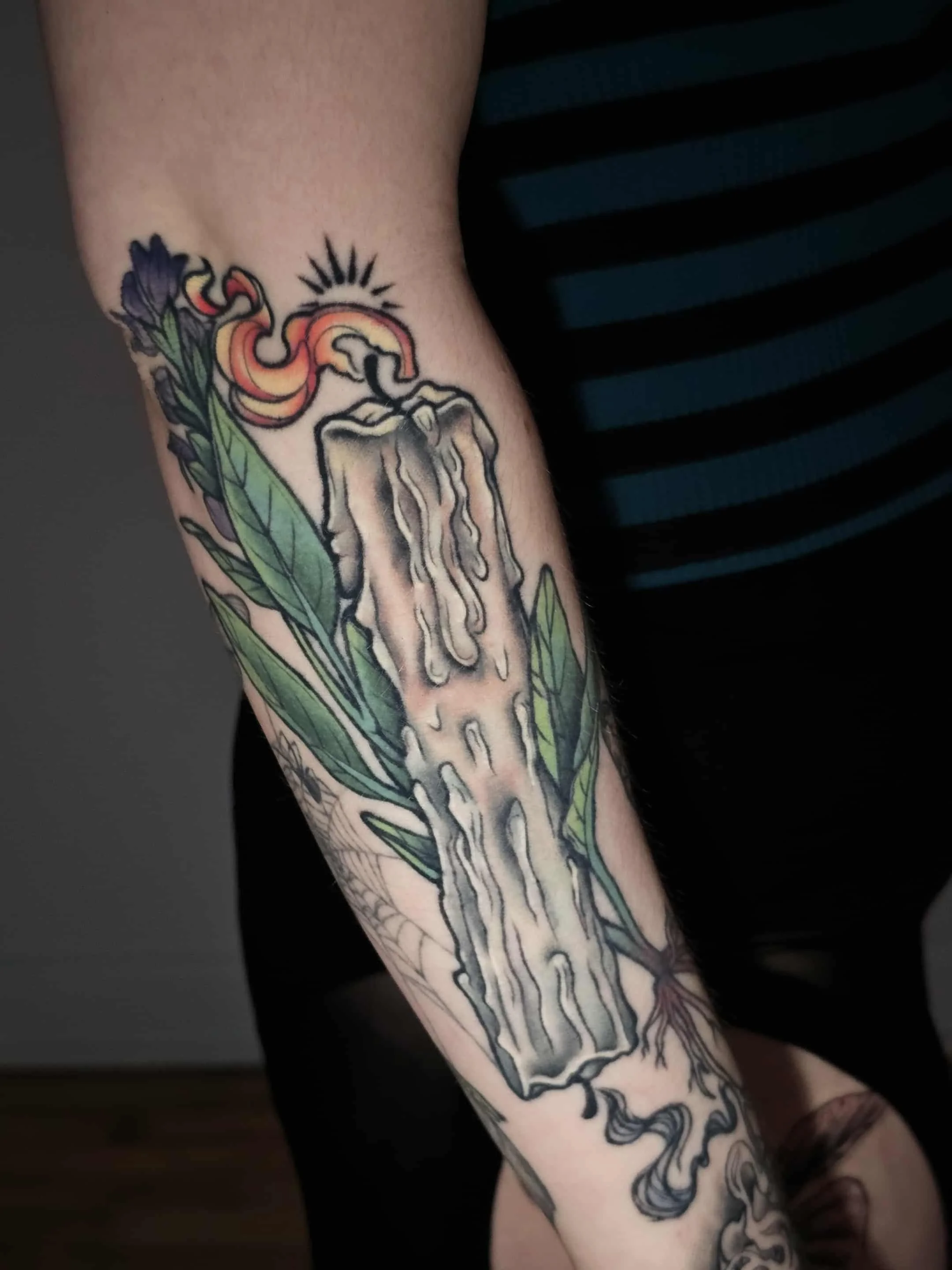 Tattoo of a melting candle with flames, surrounded by green leaves and a spider web in the lower part.