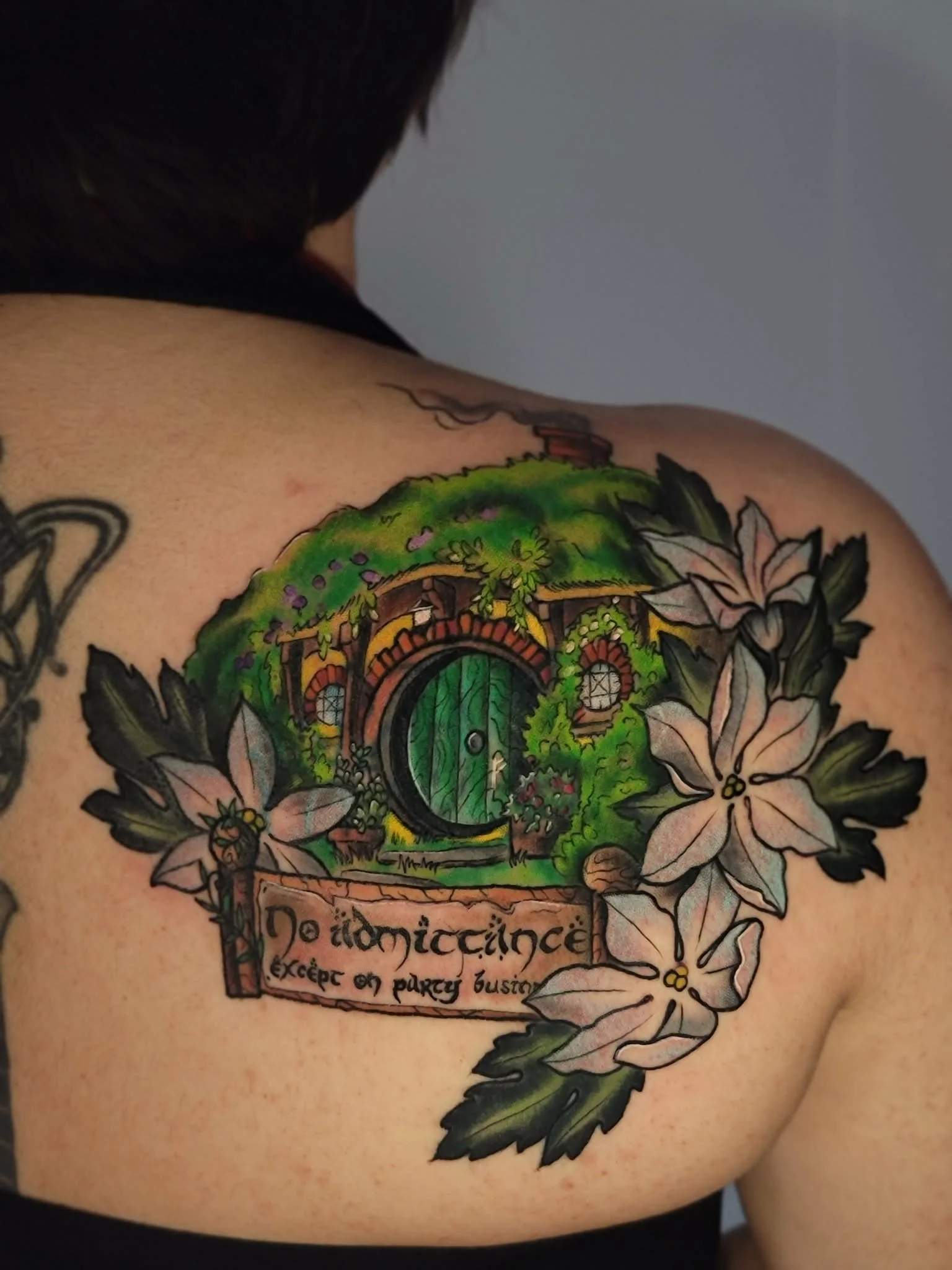 Colorful tattoo of a door surrounded by greenery and flowers, with a sign that reads 'No tiddycance' and smaller text below it.