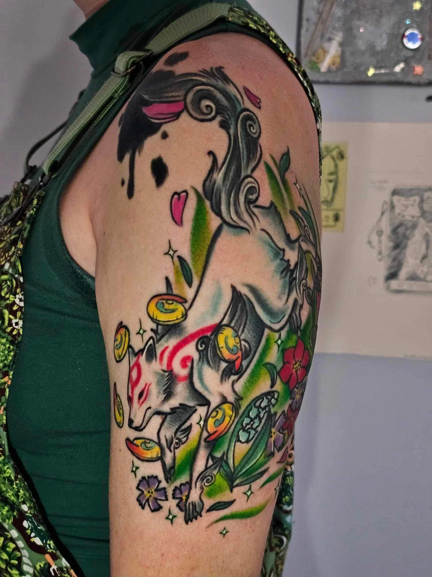 Colorful tattoo of a wolf with swirling mane, surrounded by gold coins, flowers, and green leaves on person's upper arm.